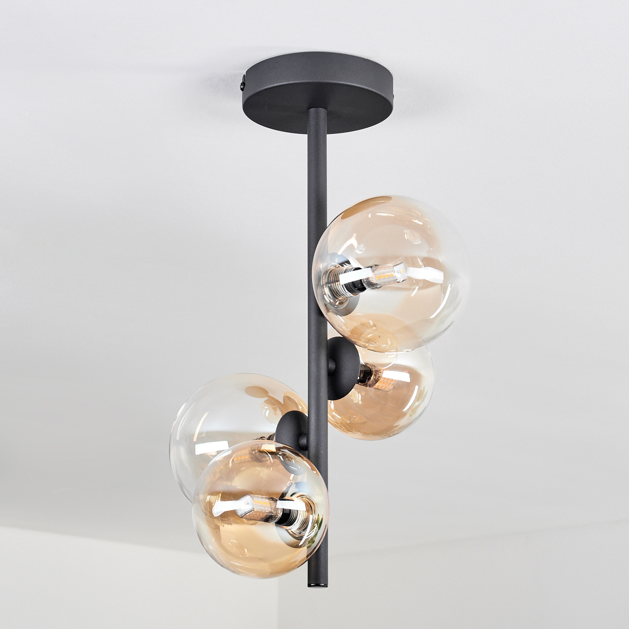 Deckenlampe mit drei bernsteinfarbenen Glaskugelleuchten. Weißer Hintergrund.