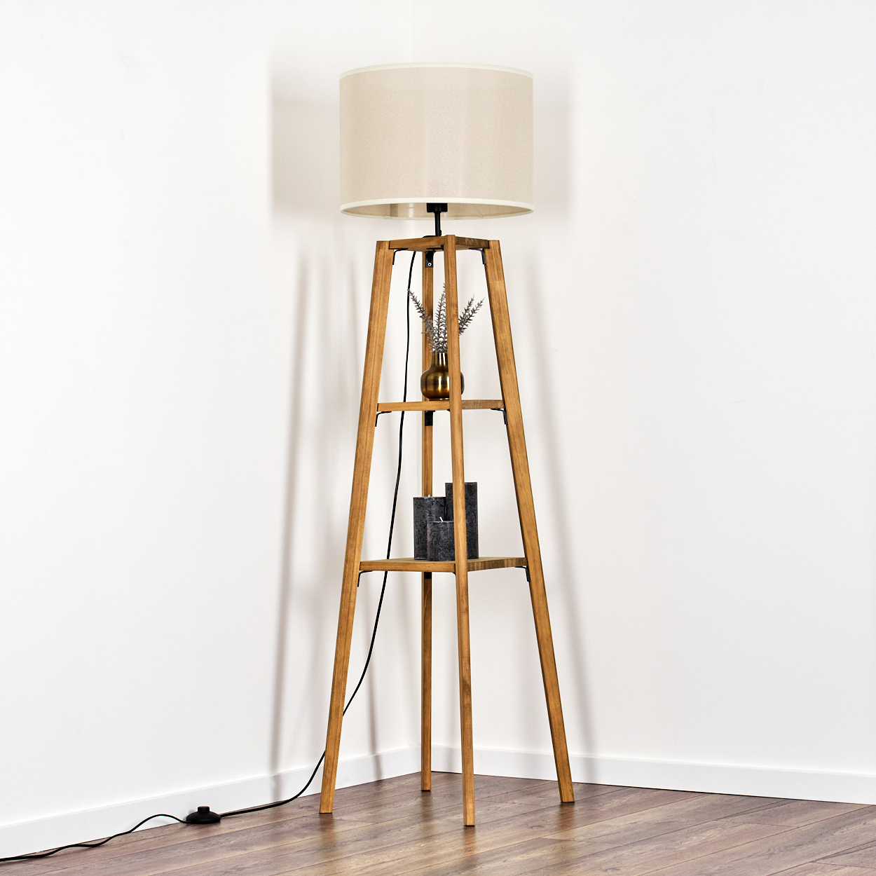Stehlampe aus Holz in der Ecke. Beiger Schirm, Holzrahmen, kleine Vase, Kerzen. Holzboden, weiße Wand.