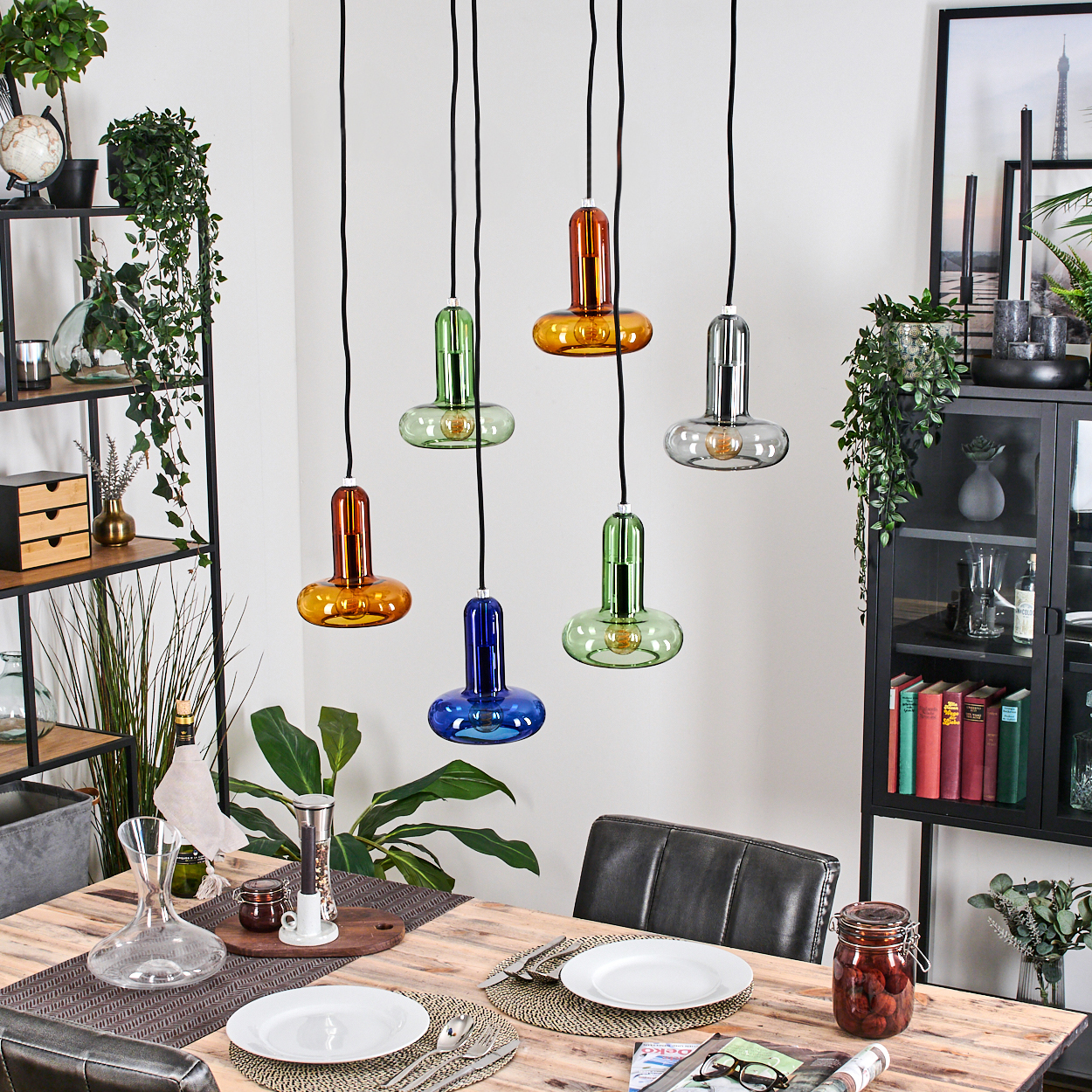 Hängeleuchten mit farbigen Glasschirmen über einem Holzesstisch-Arrangement.