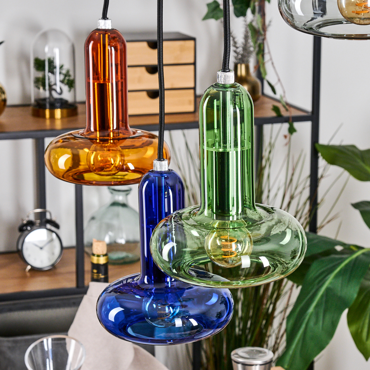 Nahaufnahme von farbenfrohen Glas-Hängeleuchten. Orange, blau und grüne Glasschirme mit sichtbaren Glühbirnen.