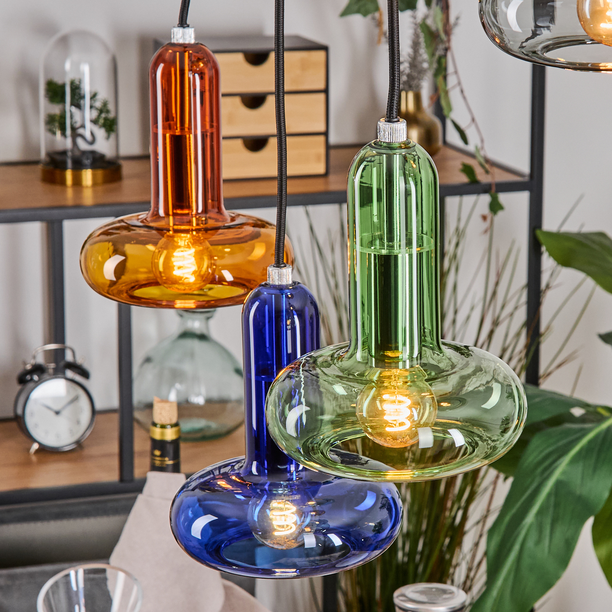 Drei bunte Glas-Pendelleuchten mit leuchtenden Glühbirnen.