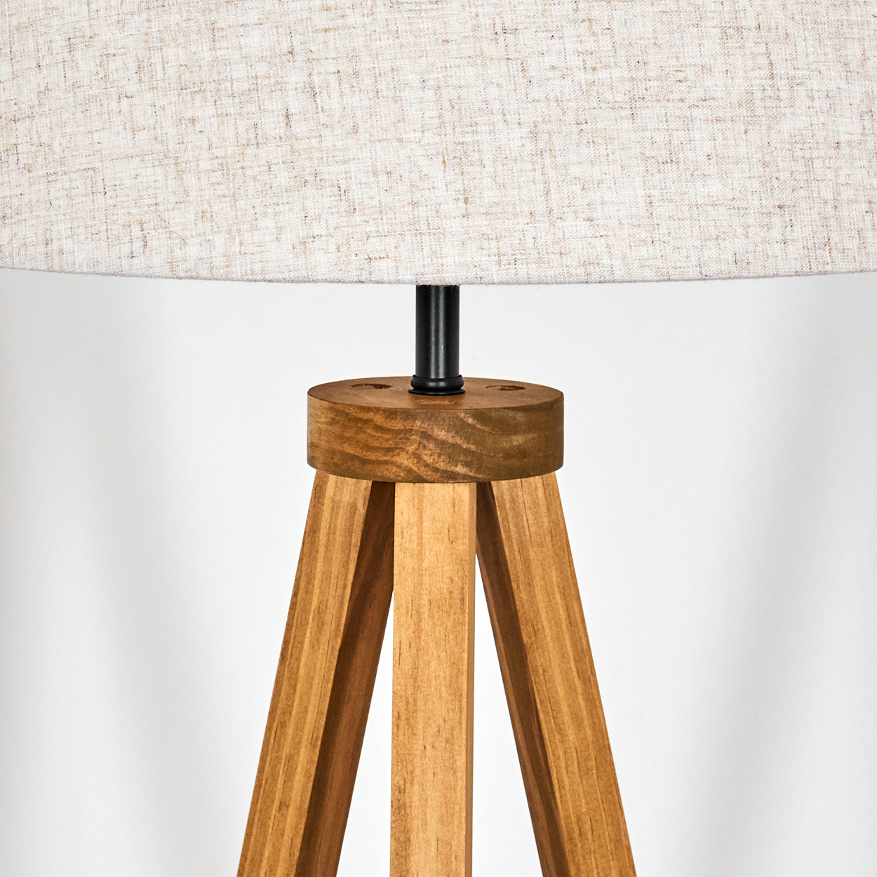 Ein hölzernes Stativgestell einer Lampe mit weißem Stoffschirm, vor weißem Hintergrund.