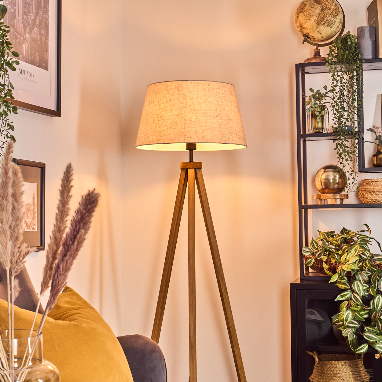 Eine Stehlampe mit Holz-Stativfuß und Stoffschirm, neben einem Regal mit Dekoration.
