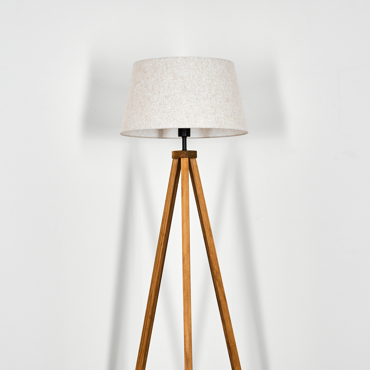 Eine Stehlampe mit Holz-Stativfuß und weißem Stoffschirm, vor weißem Hintergrund.