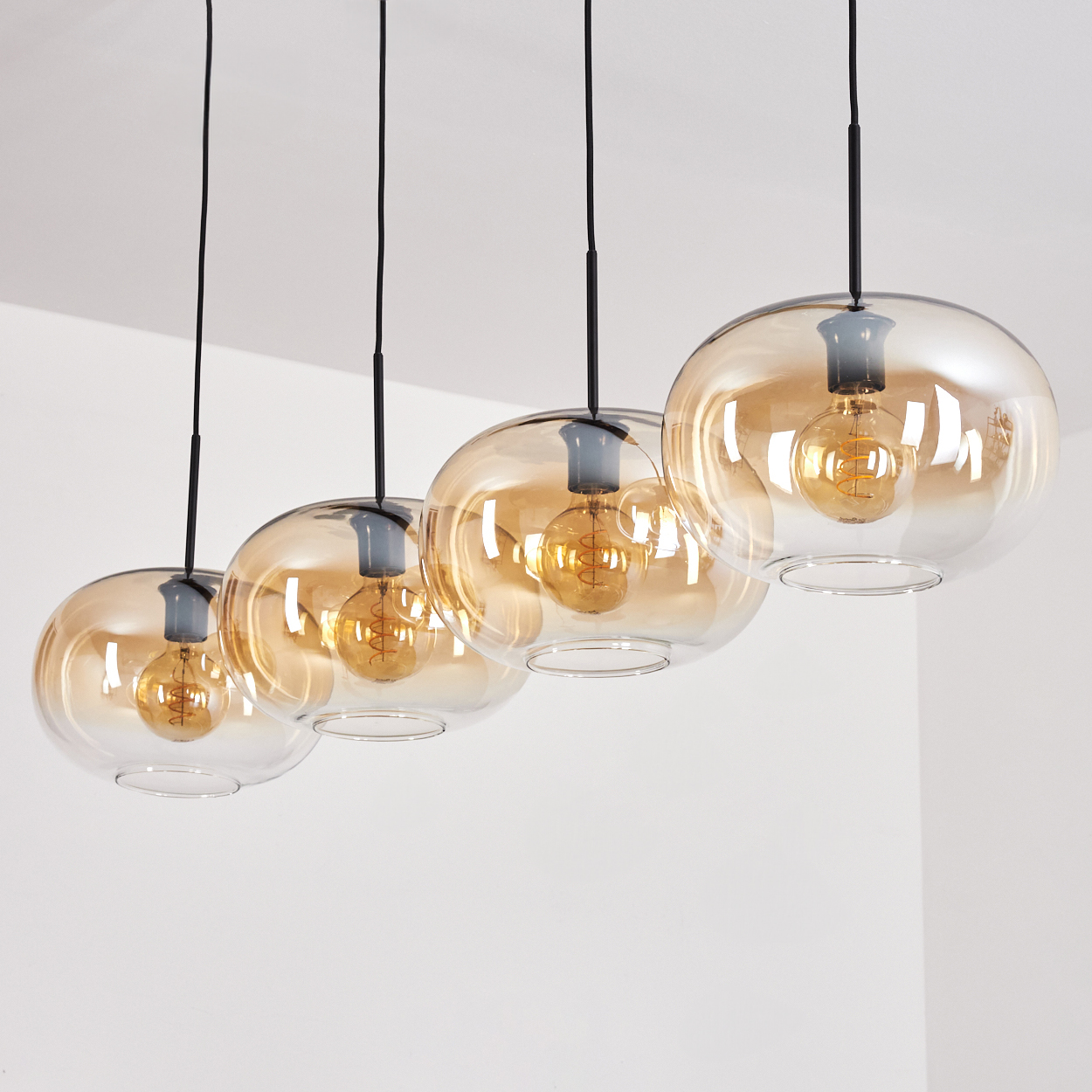 Vier Pendelleuchten mit bernsteinfarbenen Glasschirmen hängen von der Decke, beleuchtet.