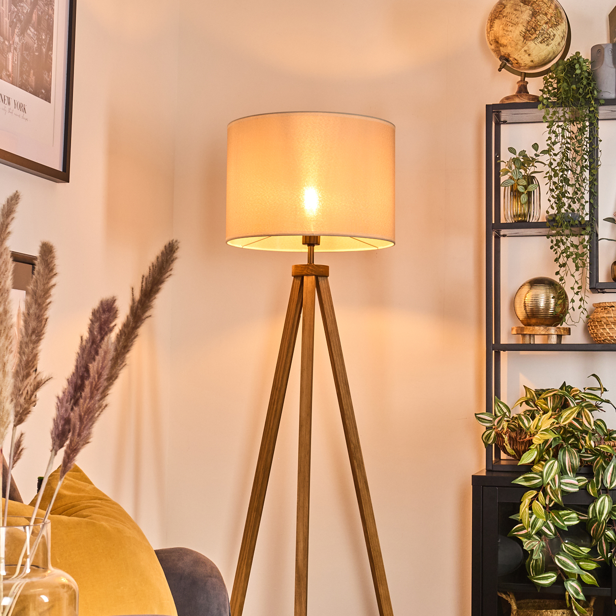 Beleuchtete Stehleuchte mit Holzstativ in einem Raum. Hintergrund: Regal mit Deko und Pflanzen. Die Lampe ist an.