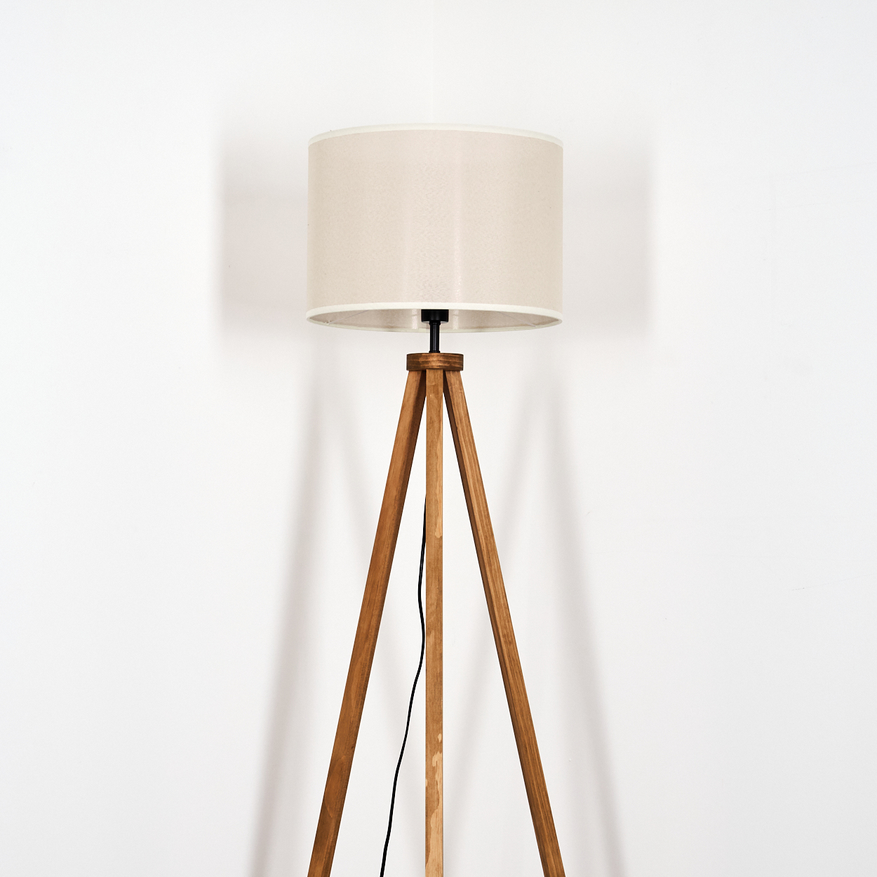 Holz-Stehlampe mit beigem Lampenschirm. Vor weißem Hintergrund.