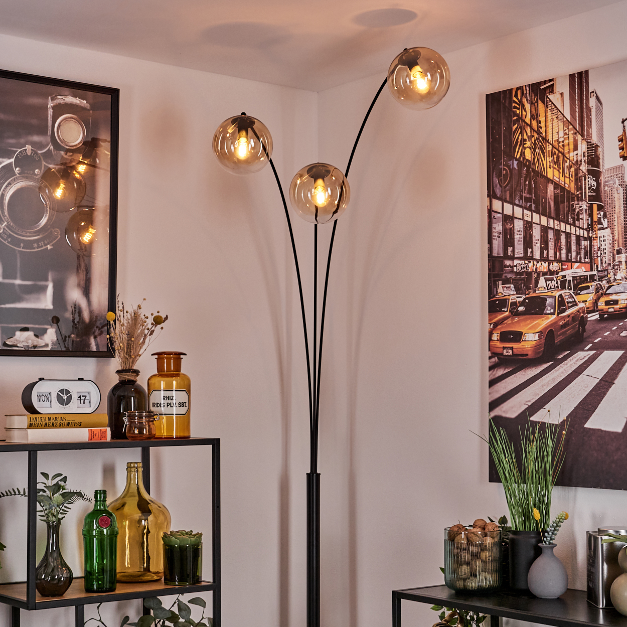 Eine schwarze Stehlampe mit drei kugelförmigen, bernsteinfarbenen Glasschirmen in einem Raum.