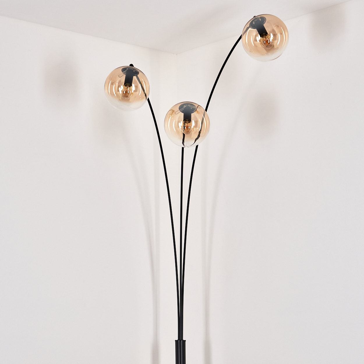 Stehlampe mit drei bernsteinfarbenen Kugelleuchten in einer Ecke, schwarzer Ständer.