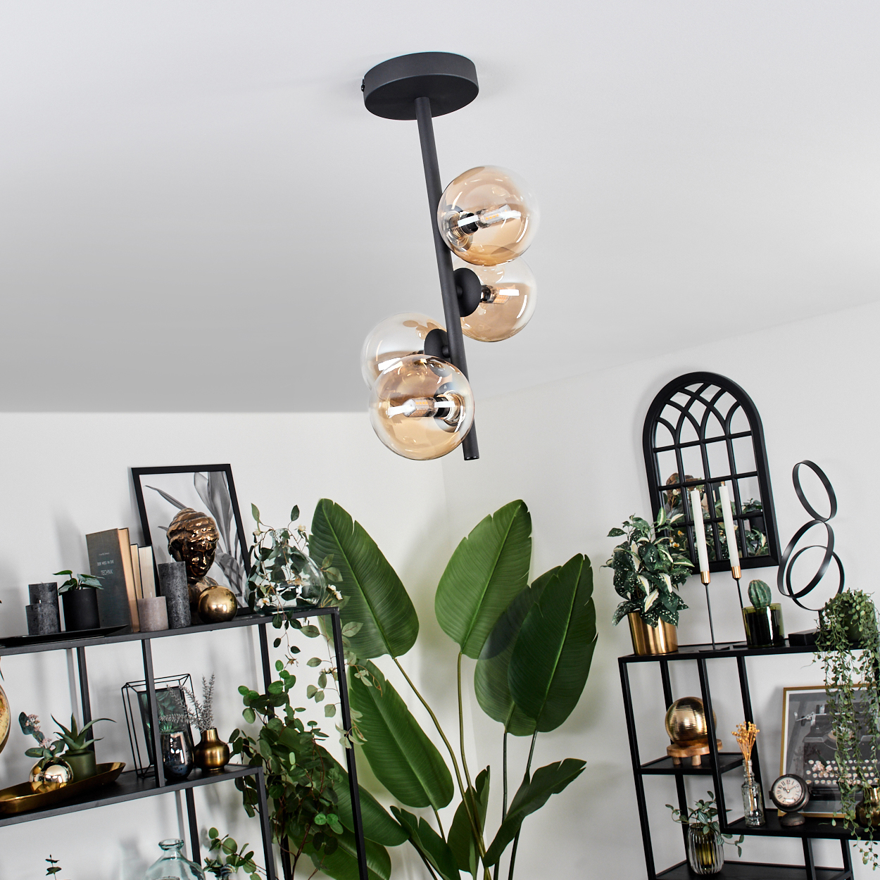 Zimmer mit schwarzen Regalen, Pflanzen und hängenden Kugelleuchten. Weiße Wand. Schwarzer Spiegel.