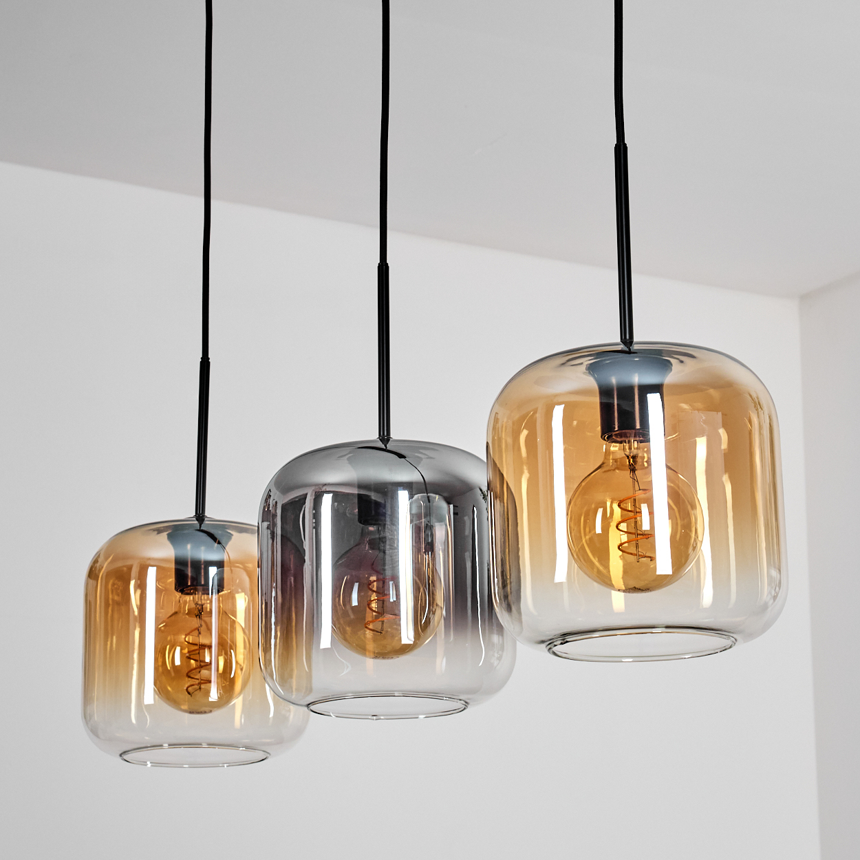 Drei Pendelleuchten mit Glasschirmen, jede mit sichtbarer Glühbirne, von der Decke hängend.