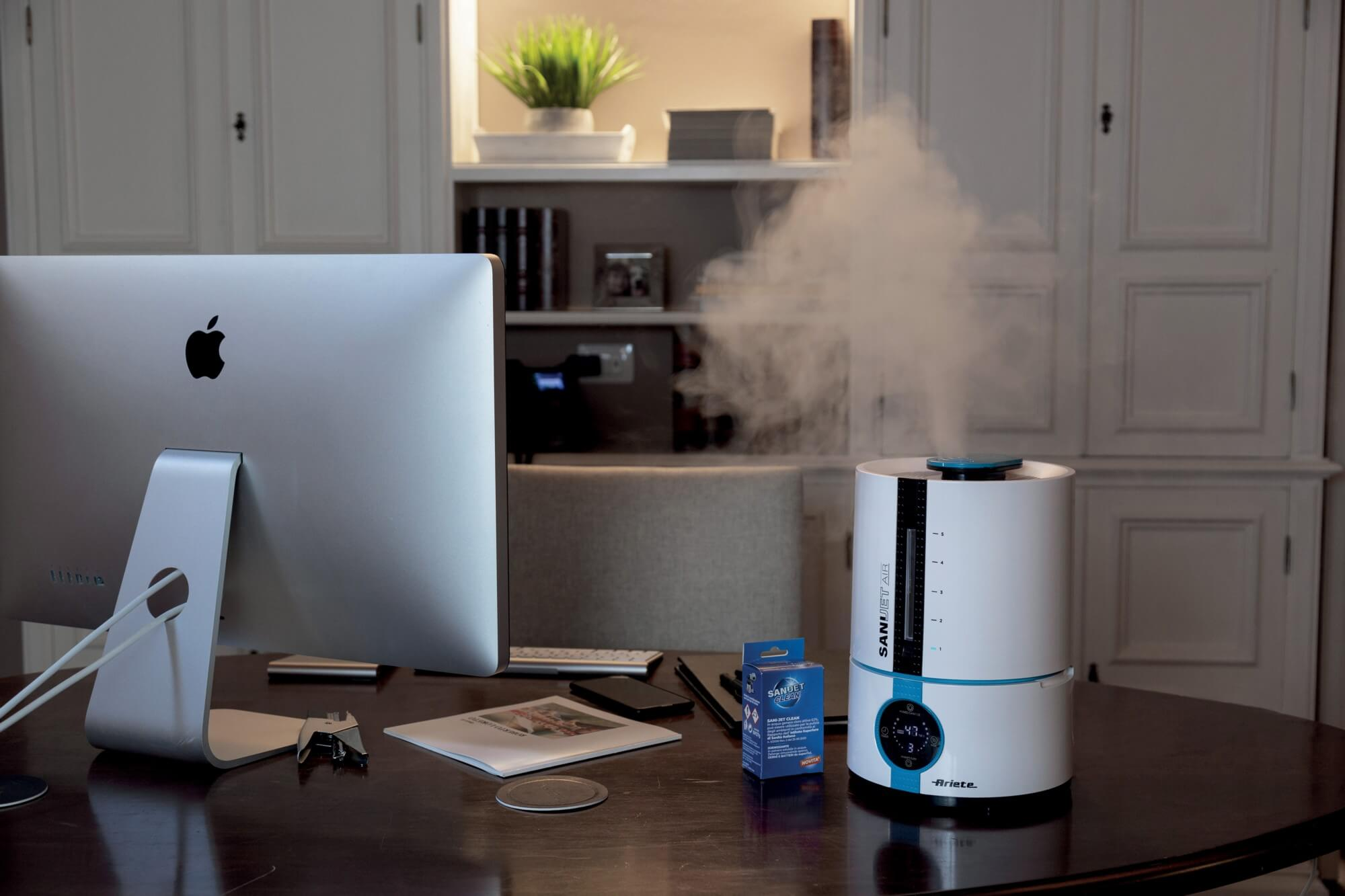 Umidificatore su una scrivania con computer, scatola di soluzione detergente e vapore.