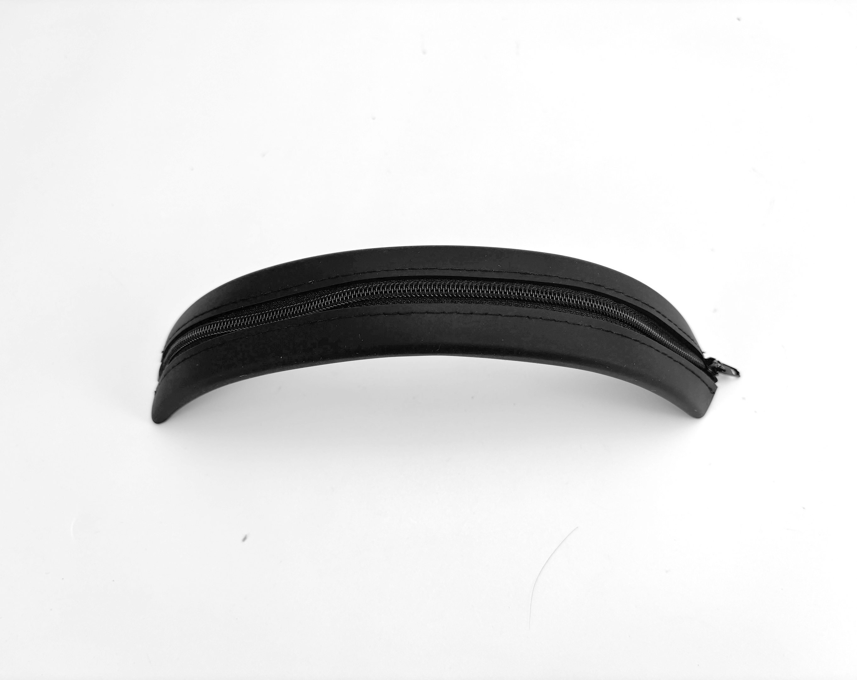 Zwarte etui met ritssluiting op een wit oppervlak. De etui is gebogen en ovaal van vorm.