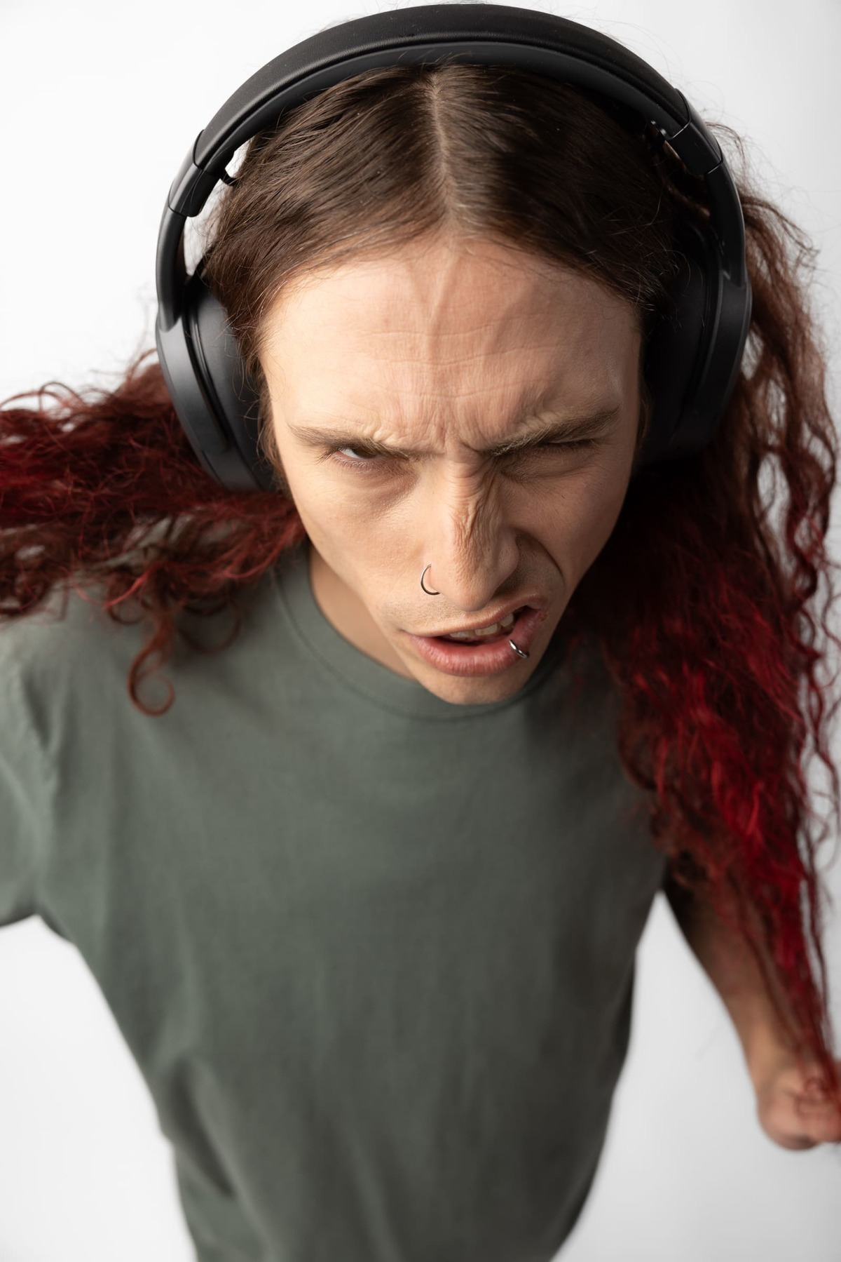 Mężczyzna w słuchawkach, ze złością. Czerwone pasemka we włosach. Białe tło.