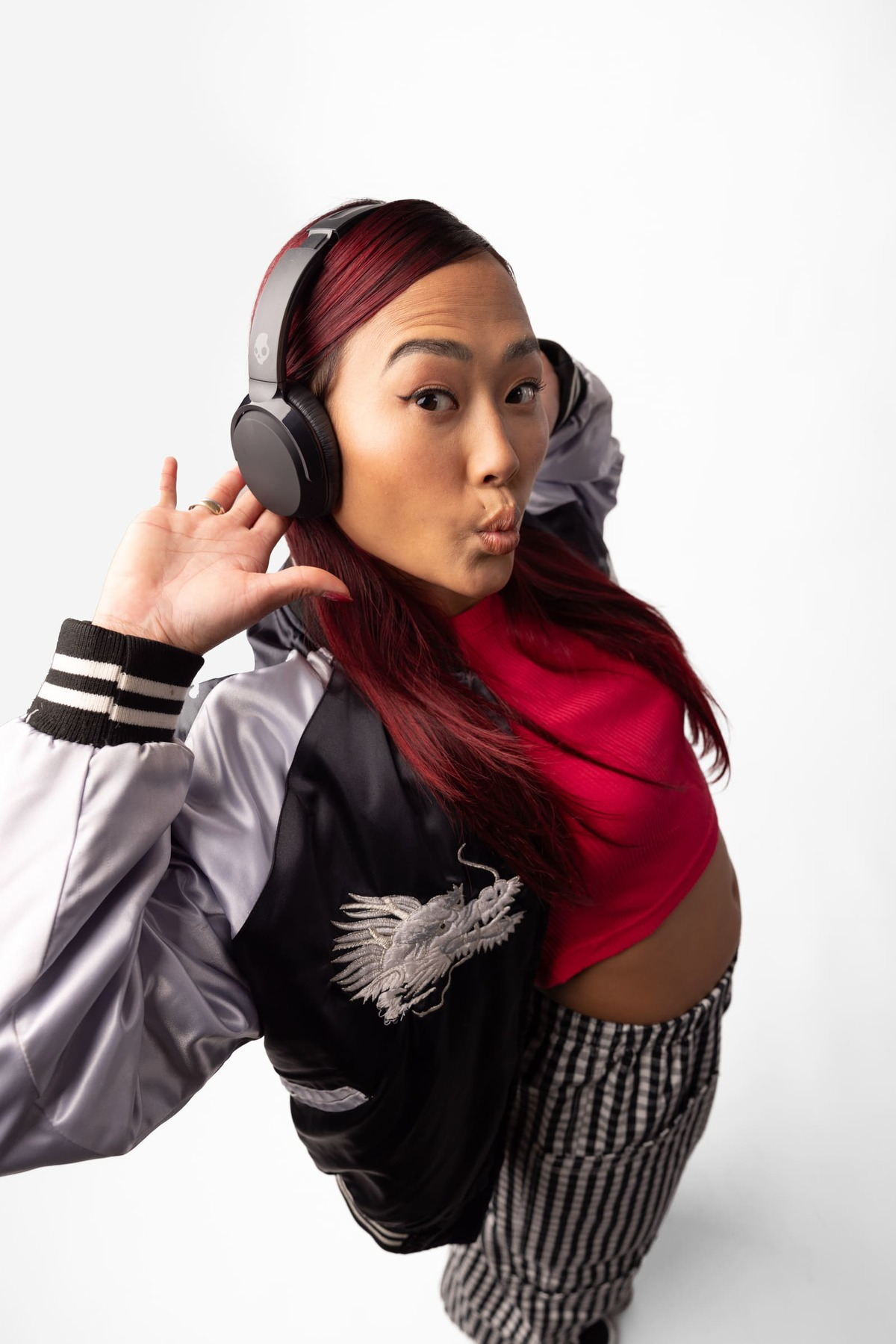 Osoba z kasztanowymi włosami w słuchawkach, kurtce bomberce i spodniach w paski.