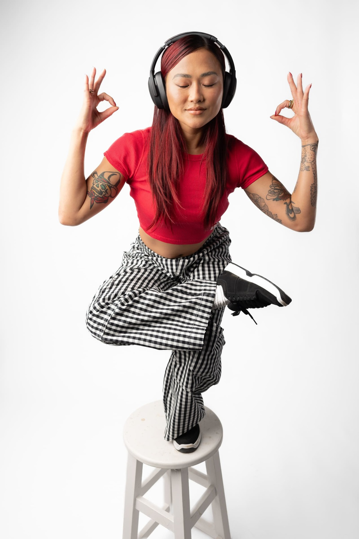 Kobieta w pozycji jogi na stołku. Ma na sobie słuchawki i czerwoną koszulę.