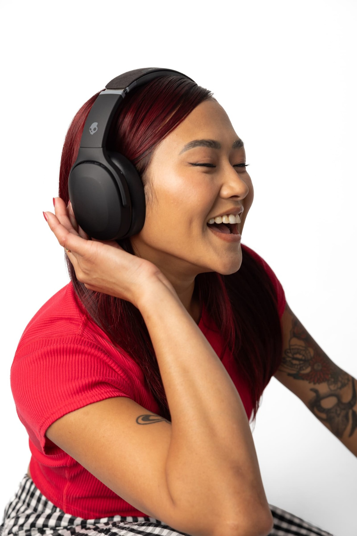 Kobieta z rudymi włosami śmieje się, ma na sobie czarne słuchawki i czerwoną koszulę.