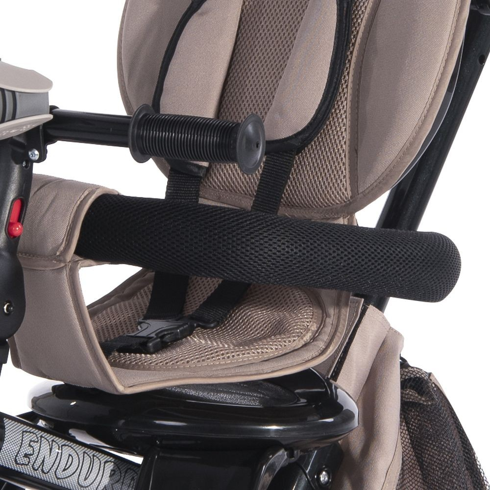 Primer plano del manillar de un triciclo. Es negro con un asiento beige. Fondo blanco.