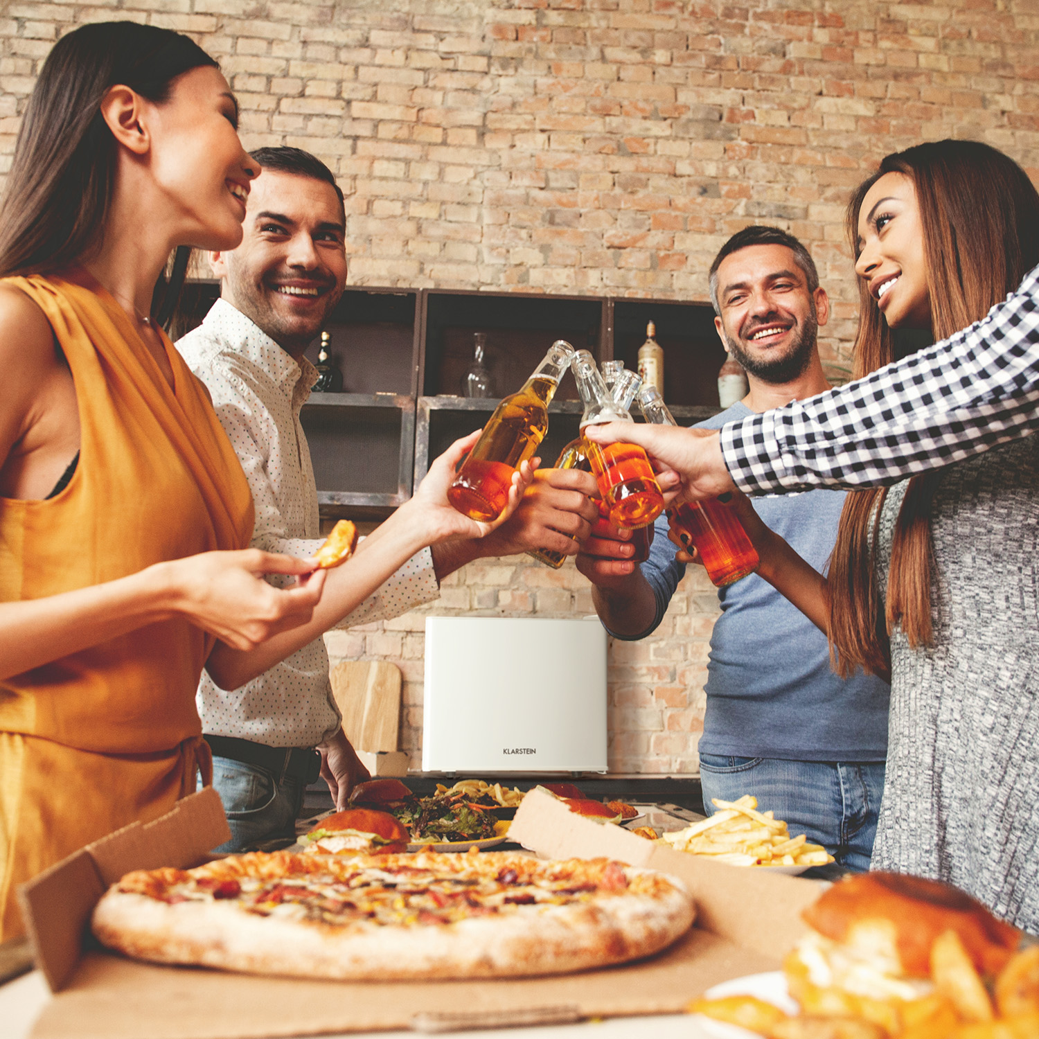 Eine Gruppe von Personen, die mit Bierflaschen anstoßen, nahe Pizza und Heizung.