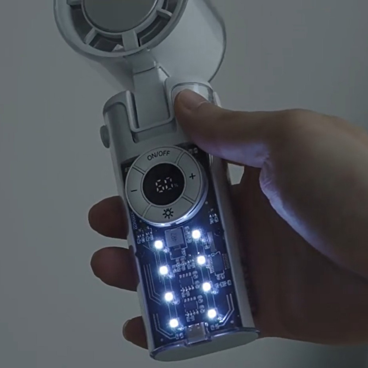 Mano che tiene un dispositivo che mostra un circuito stampato, con pulsanti di accensione/spegnimento e controllo, e luci a LED.