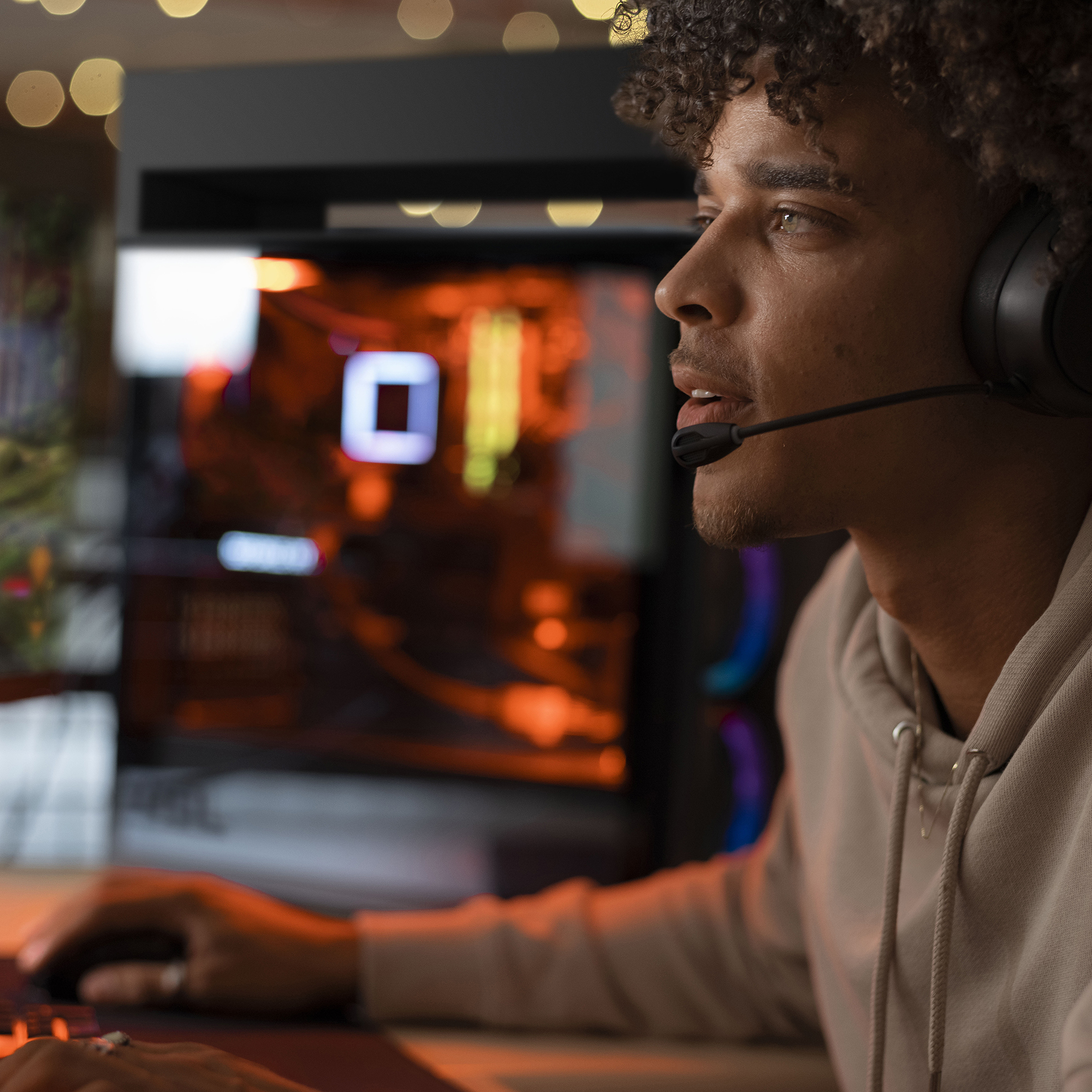 Mężczyzna w zestawie słuchawkowym, patrzący na ekran komputera podczas grania, z obudową komputera w tle.