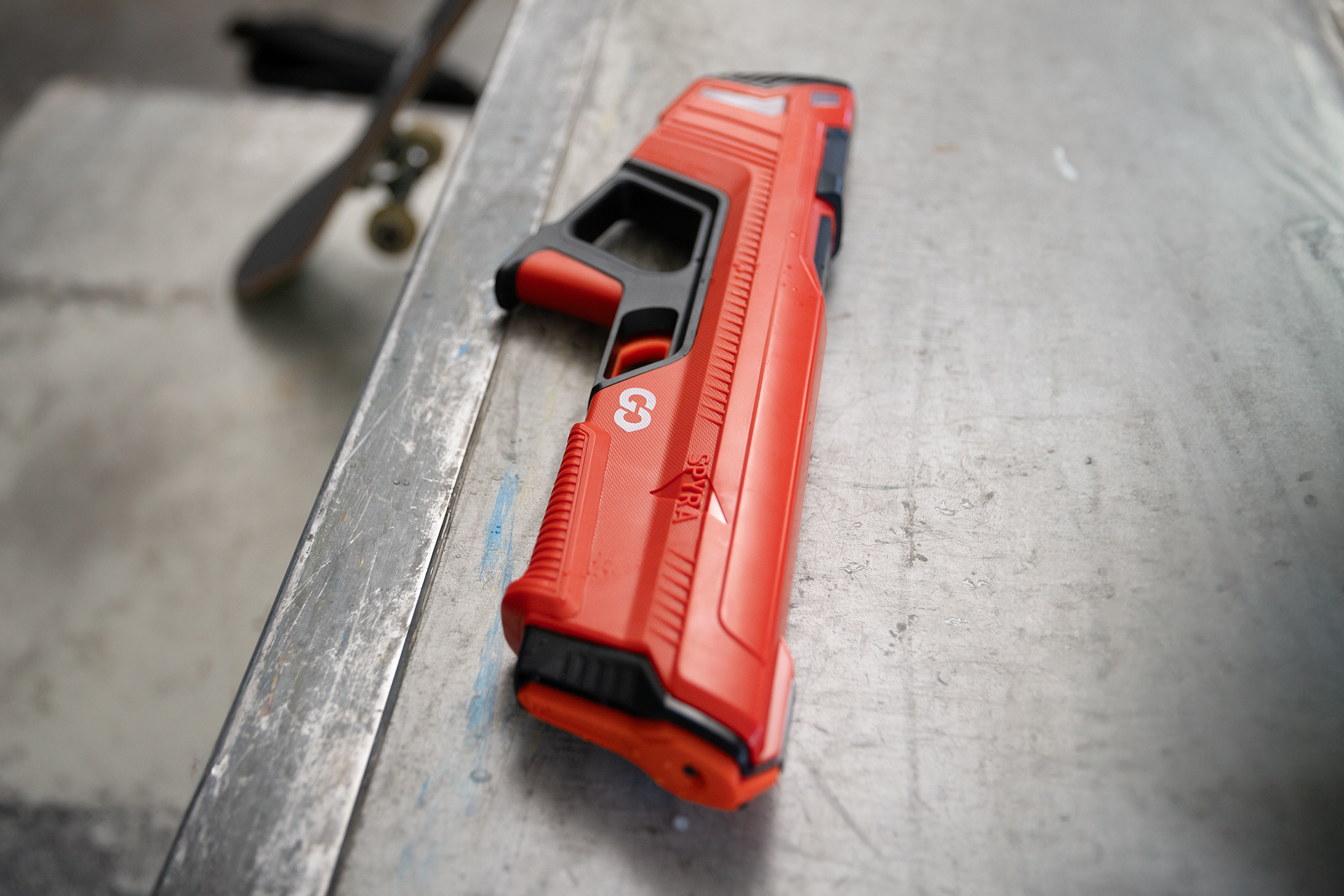Eine rote Wasserpistole liegt auf einer Metalloberfläche. Ein schwarzer Griff und Abzug sind sichtbar.