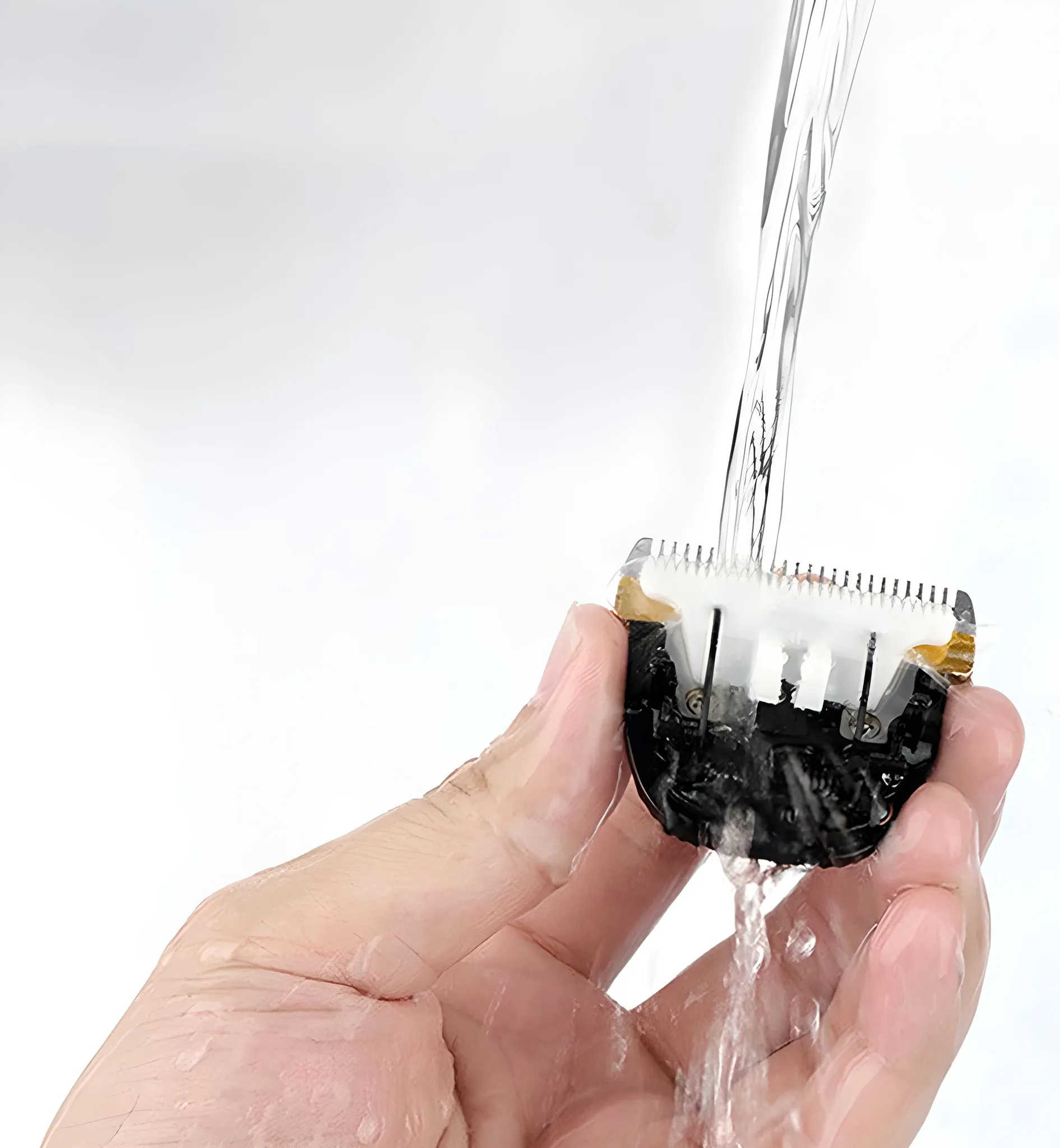 Eine Hand spült eine Tierpflege-Schermaschinenklinge unter fließendem Wasser, weißer Hintergrund.