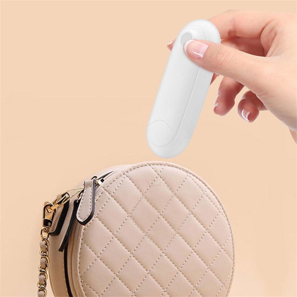 Eine Hand hält ein weißes, ovales Gerät in der Nähe einer beigen Handtasche.