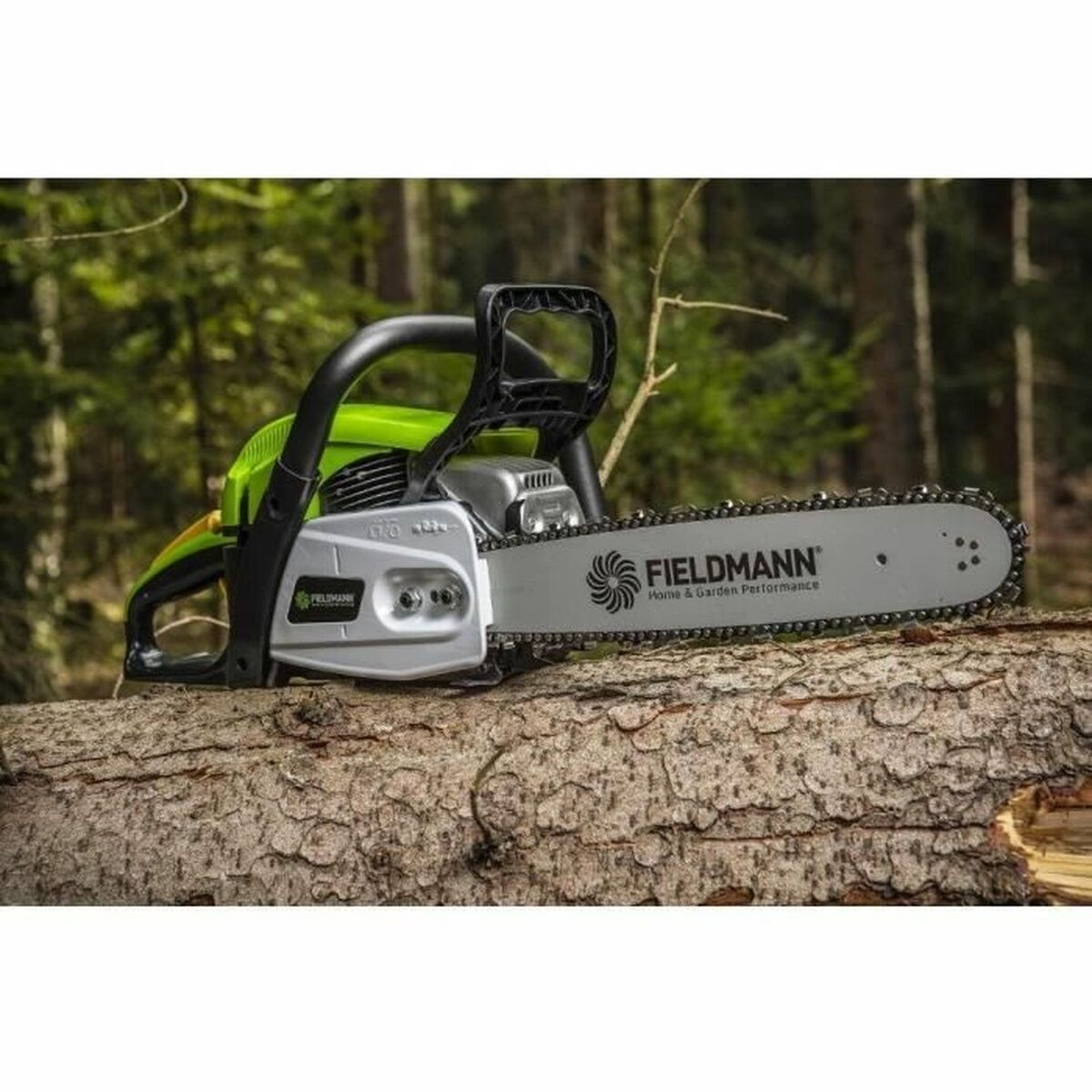 Grüne und silberne Kettensäge auf einem Baumstamm. FIELDMANN-Logo sichtbar. Wald im Hintergrund.