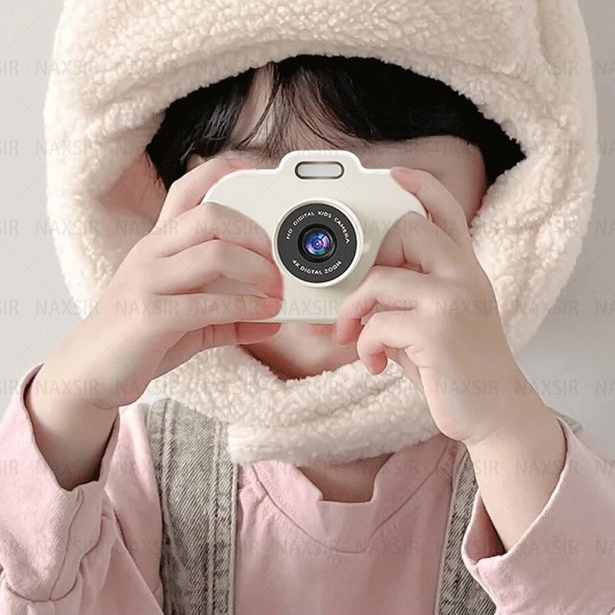 Un bambino con un cappuccio peloso, che tiene una fotocamera bianca per bambini, scattando una foto, al chiuso, primo piano.