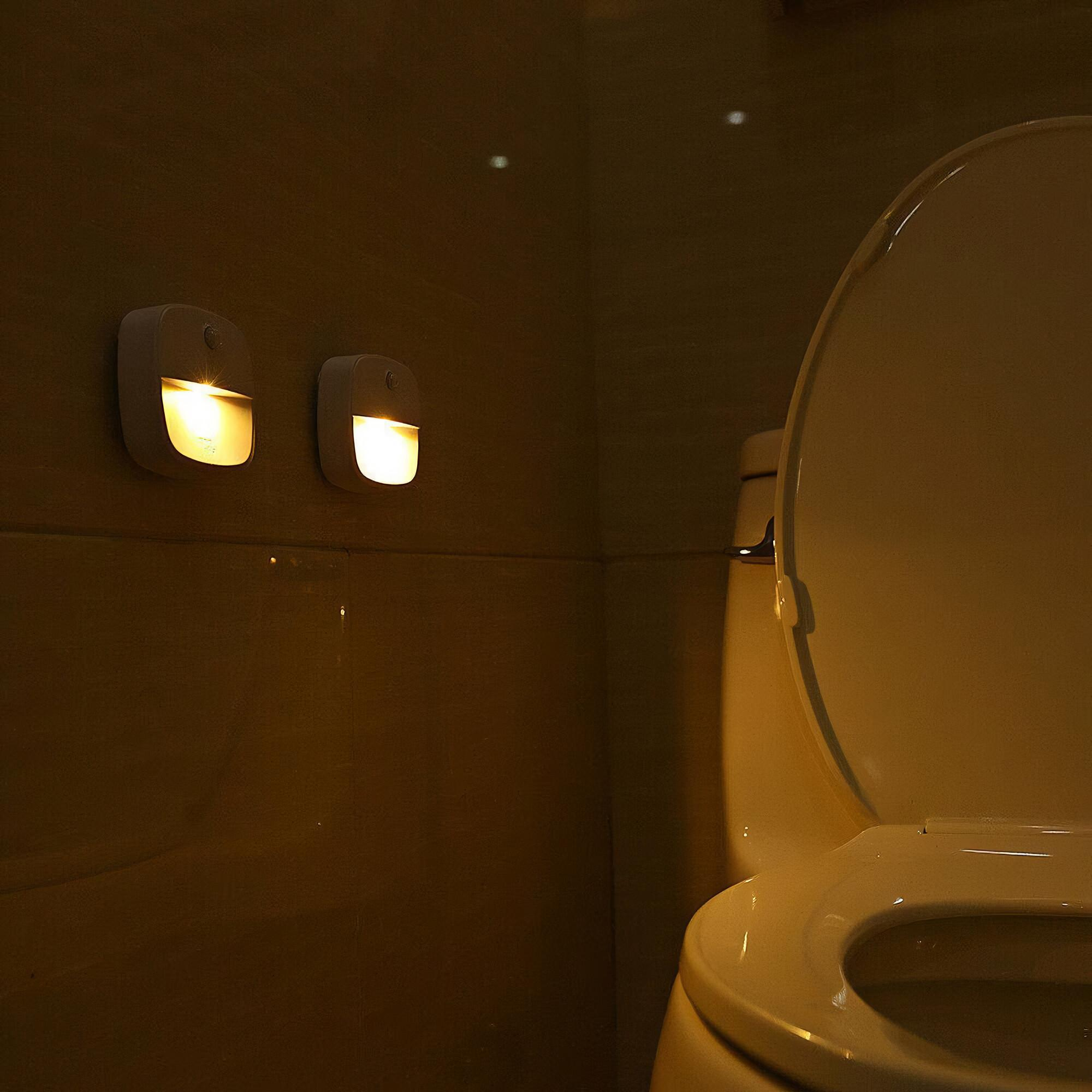 Zwei weiße Nachtlichter an einer Wand neben einer Toilette.