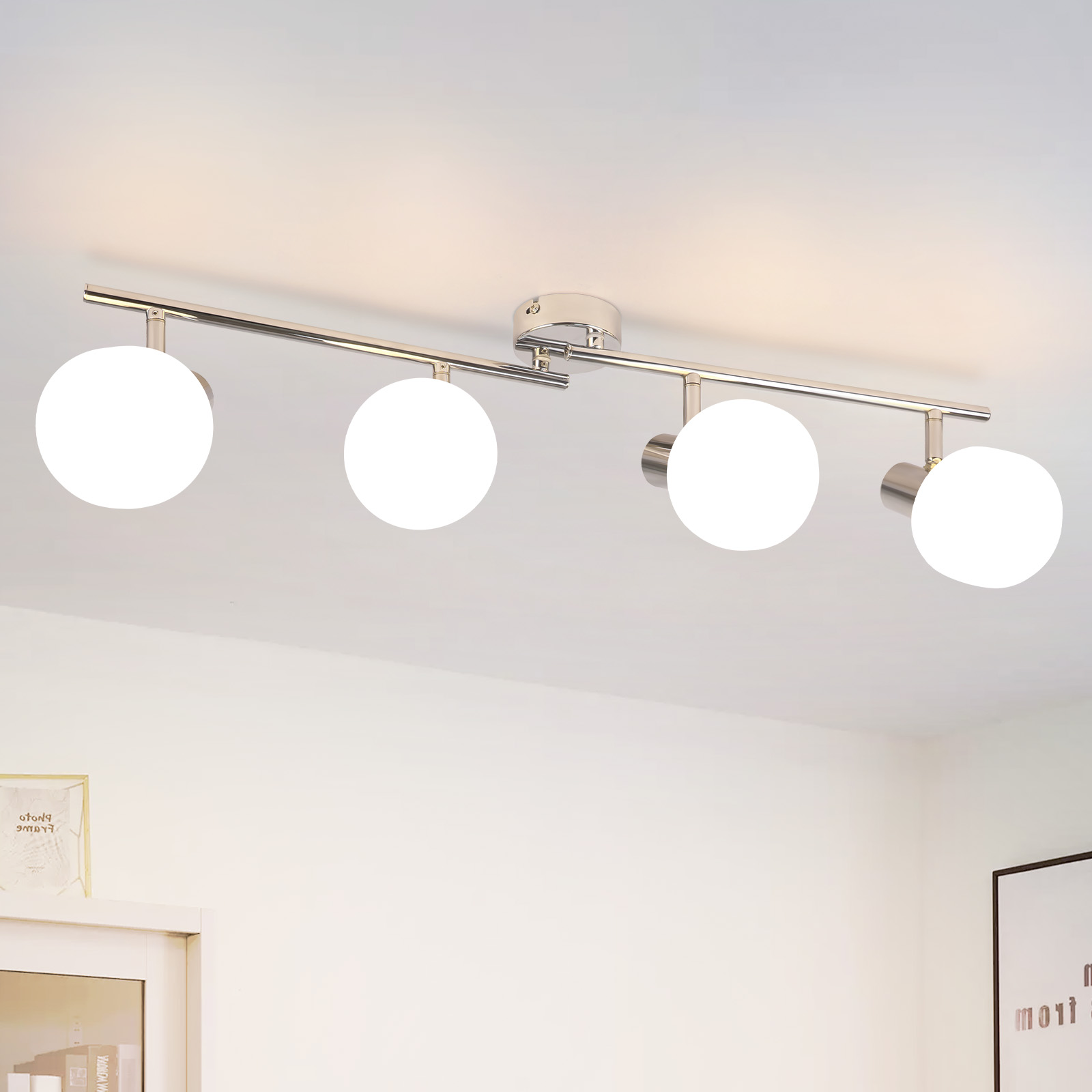 Un apparecchio di illuminazione a soffitto con quattro luci a globo bianche contro un soffitto bianco. L'apparecchio è argentato.