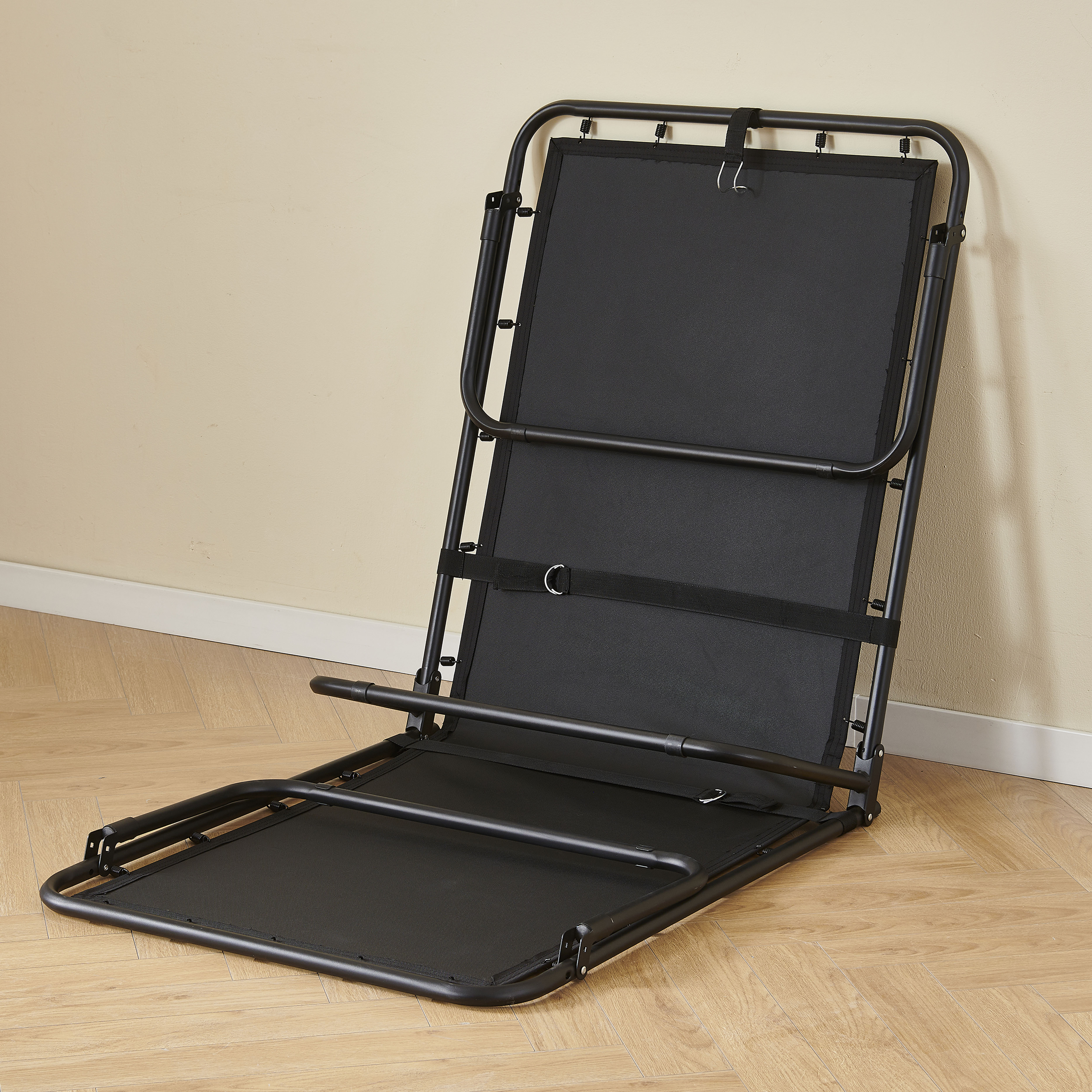 Klappbarer schwarzer Stuhl mit schwarzer Sitzfläche und Rückenlehne, an beiger Wand.
