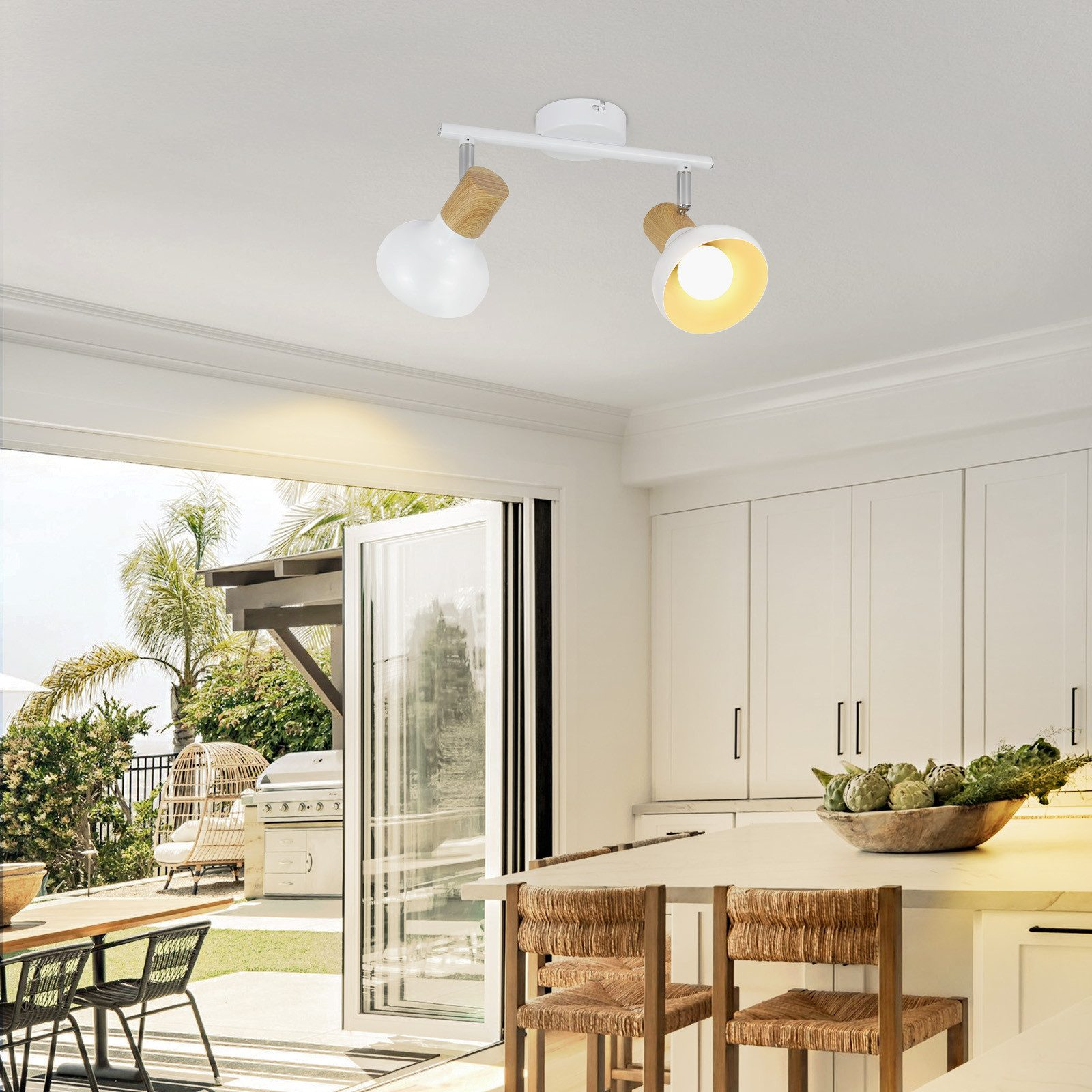 Cucina con luci a soffitto. Armadi, isola e tavolo bianchi. Porta aperta sul patio.