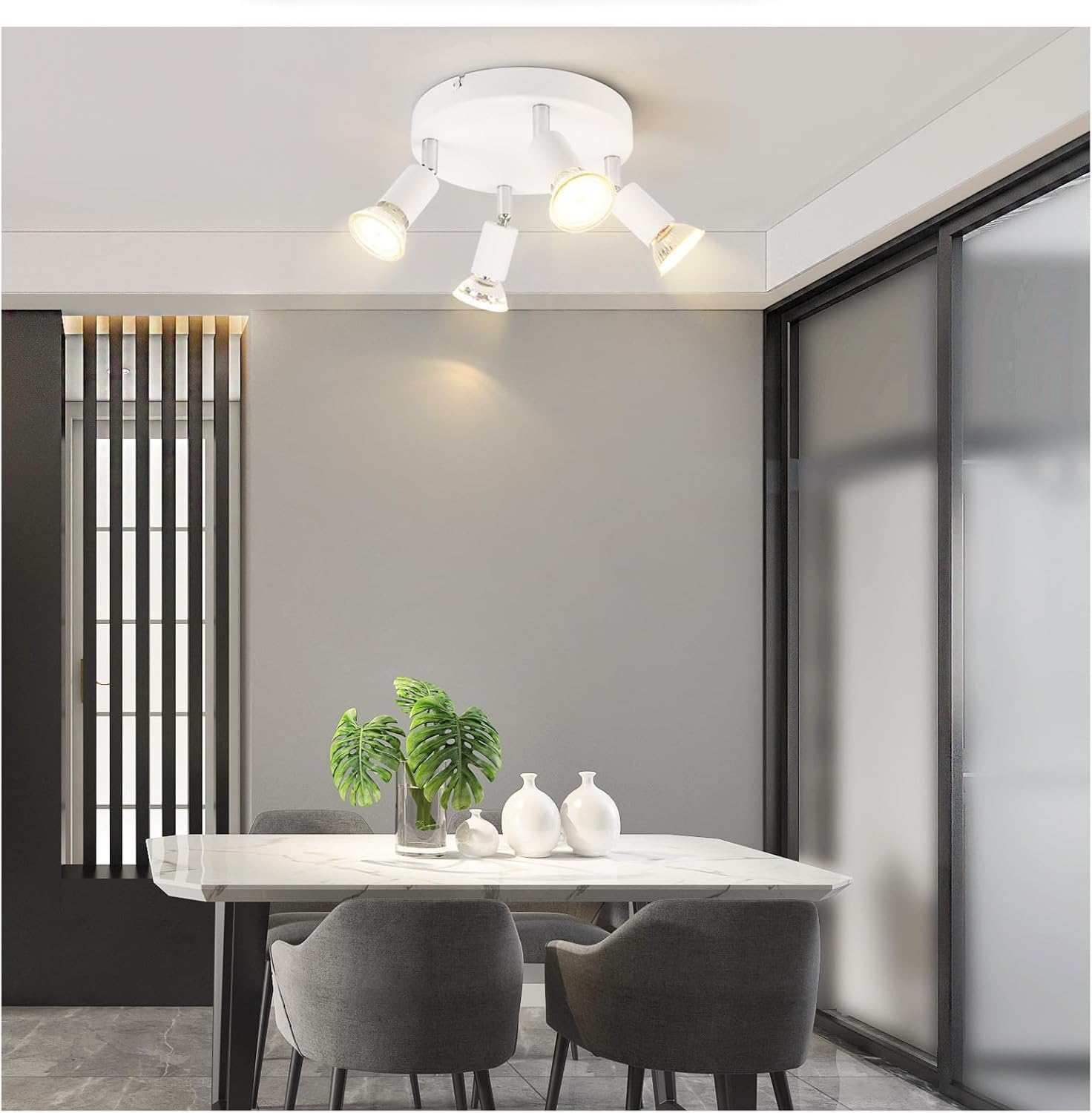 Sala da pranzo con faretti a soffitto. Tavolo con piante e vasi. Sedie grigie visibili.