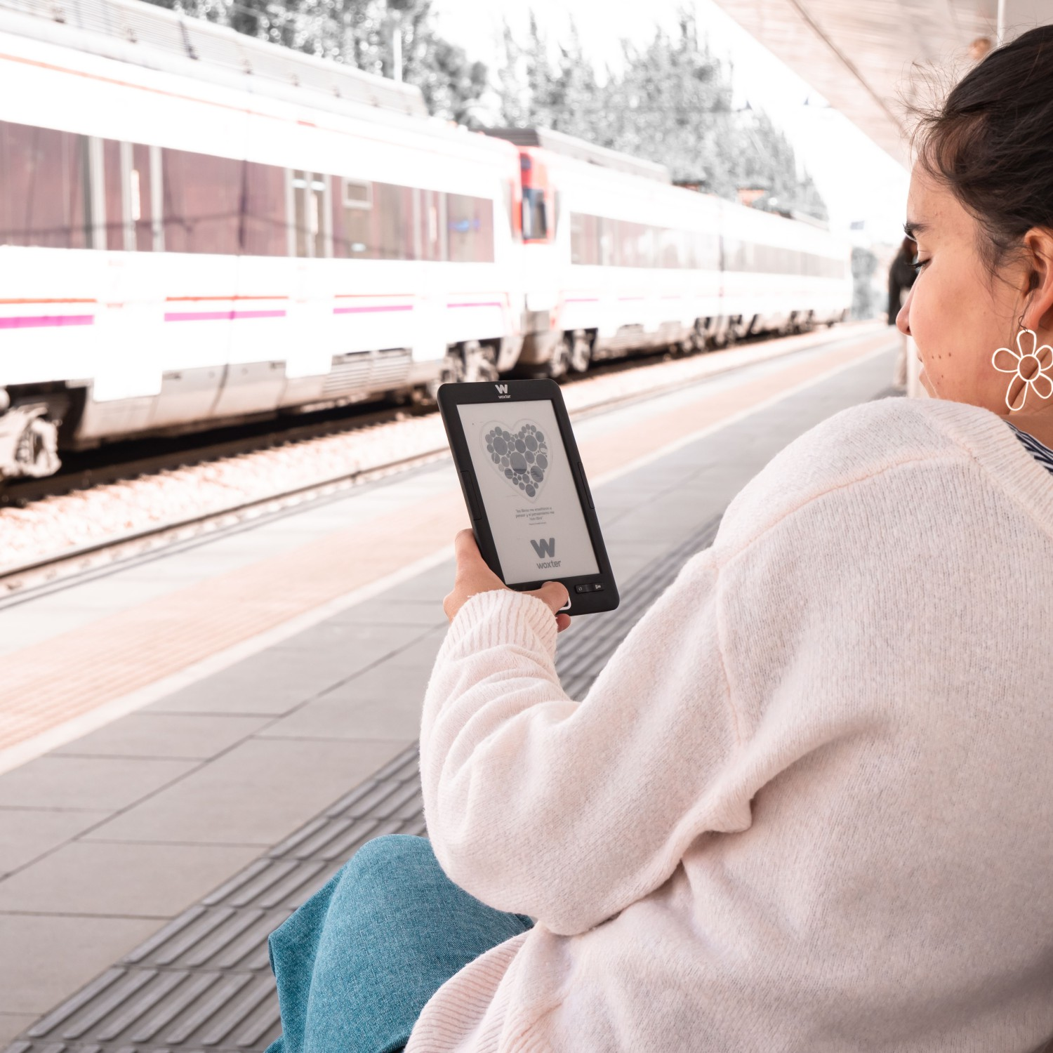 Kobieta na peronie, trzyma czytnik. Pociąg przejeżdża w tle.