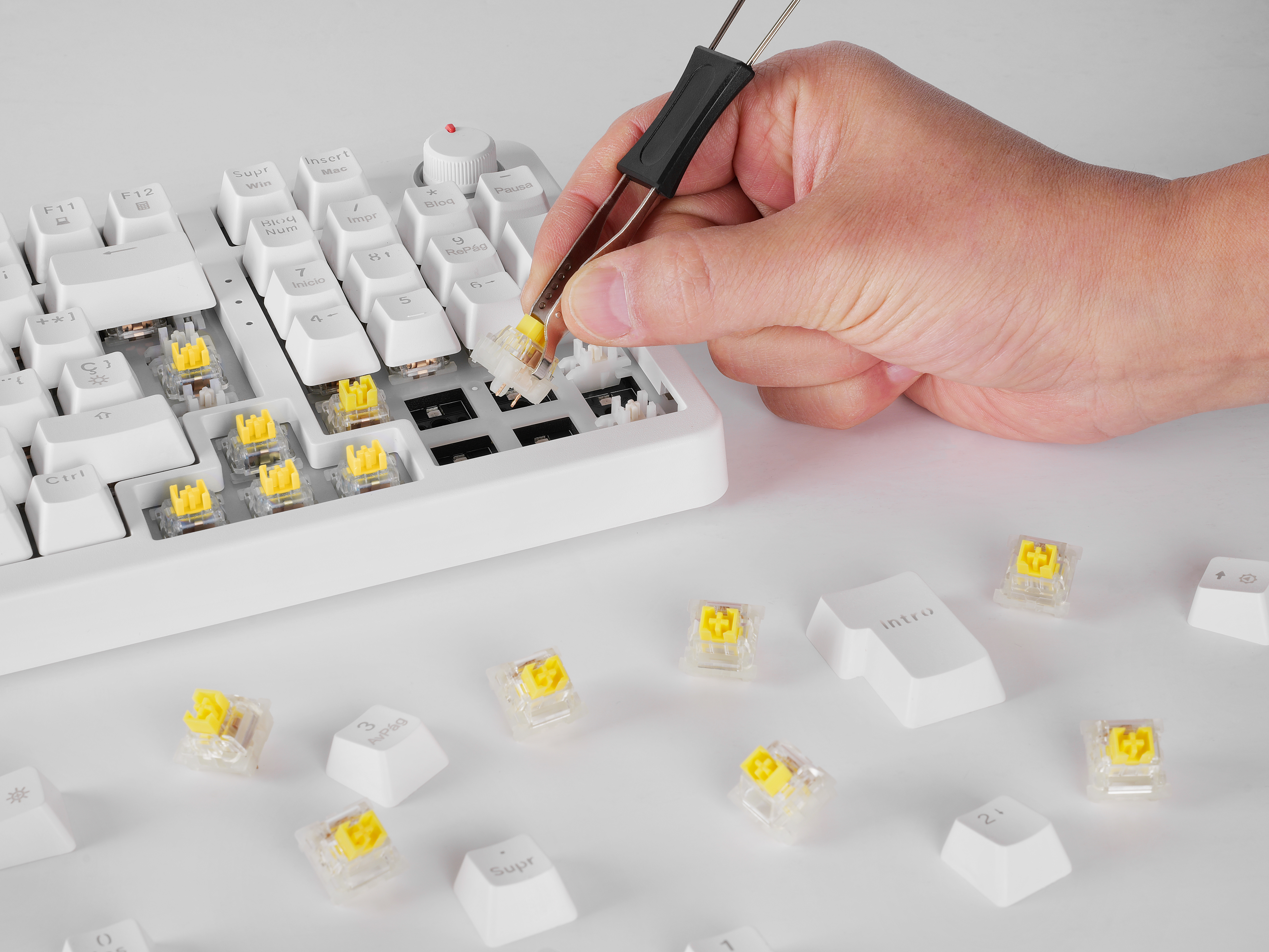 Hand benutzt Pinzette, um einen gelben Schalter von einer weißen mechanischen Tastatur zu entfernen.