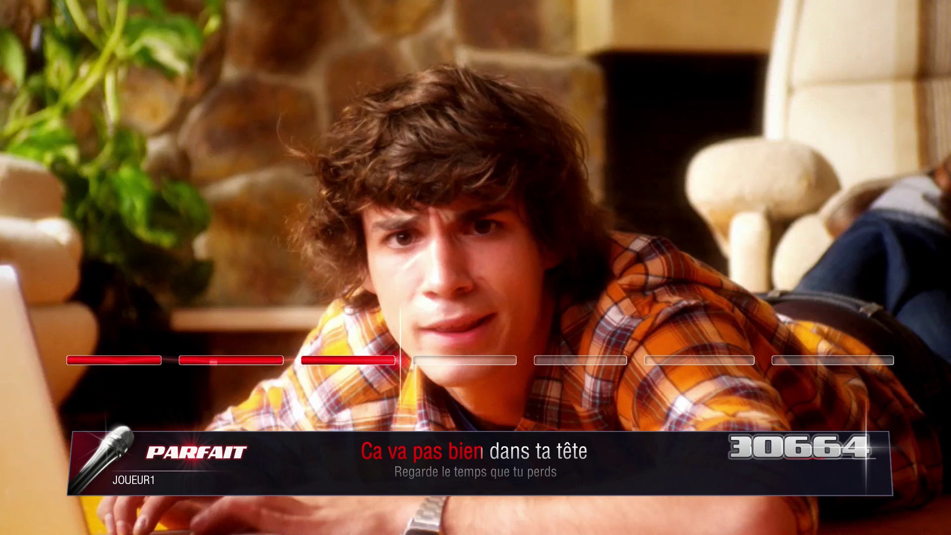 Mężczyzna w koszuli w kratę śpiewa z interfejsem gry karaoke na ekranie.