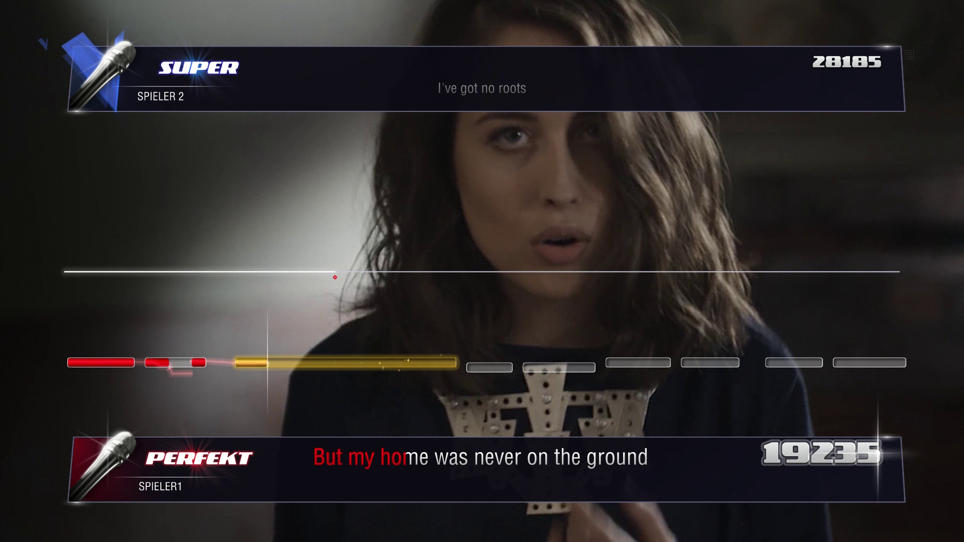 Kobieta śpiewa na scenie z interfejsem gry na dole. Tło jest rozmyte.