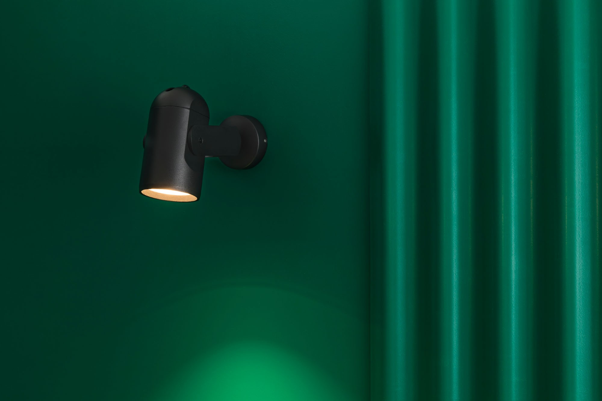 Una luce nera a parete brilla su un muro verde. Il muro ha creste verticali.
