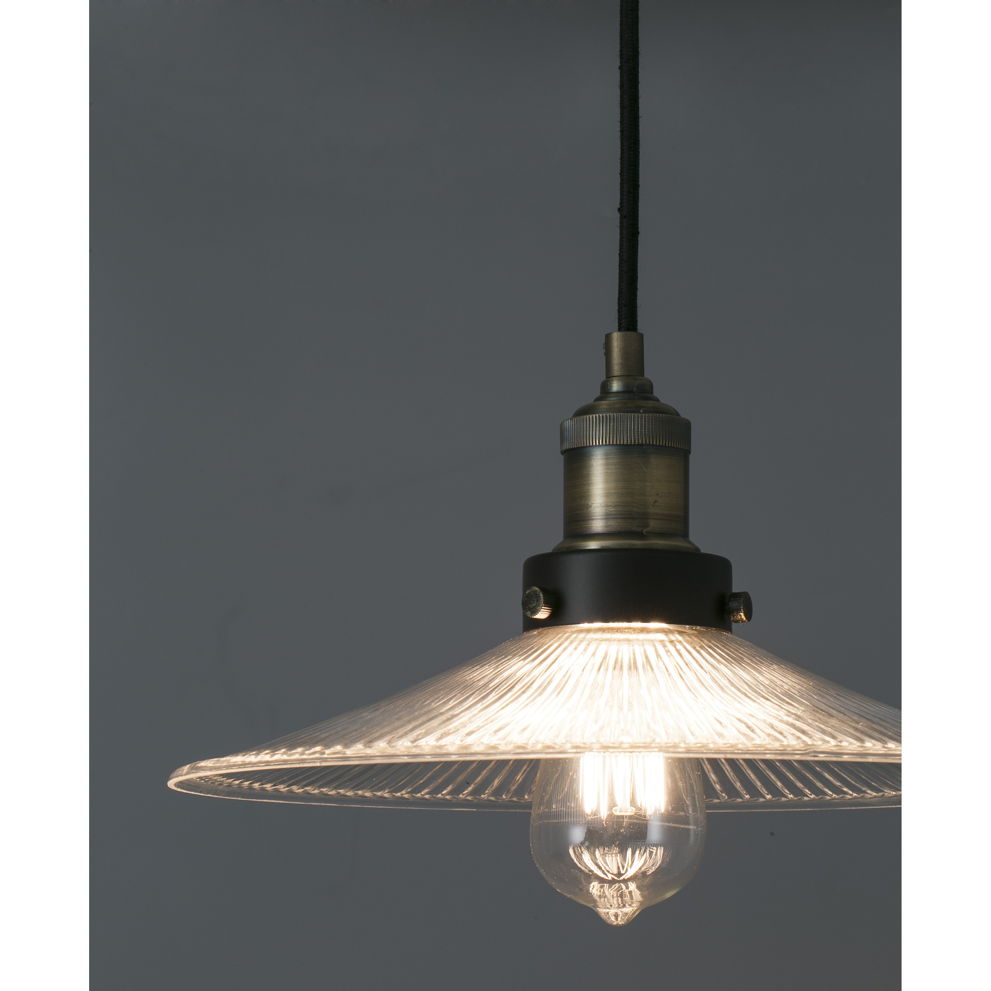 Lampada a sospensione con paralume in vetro, che emette luce, su sfondo grigio.