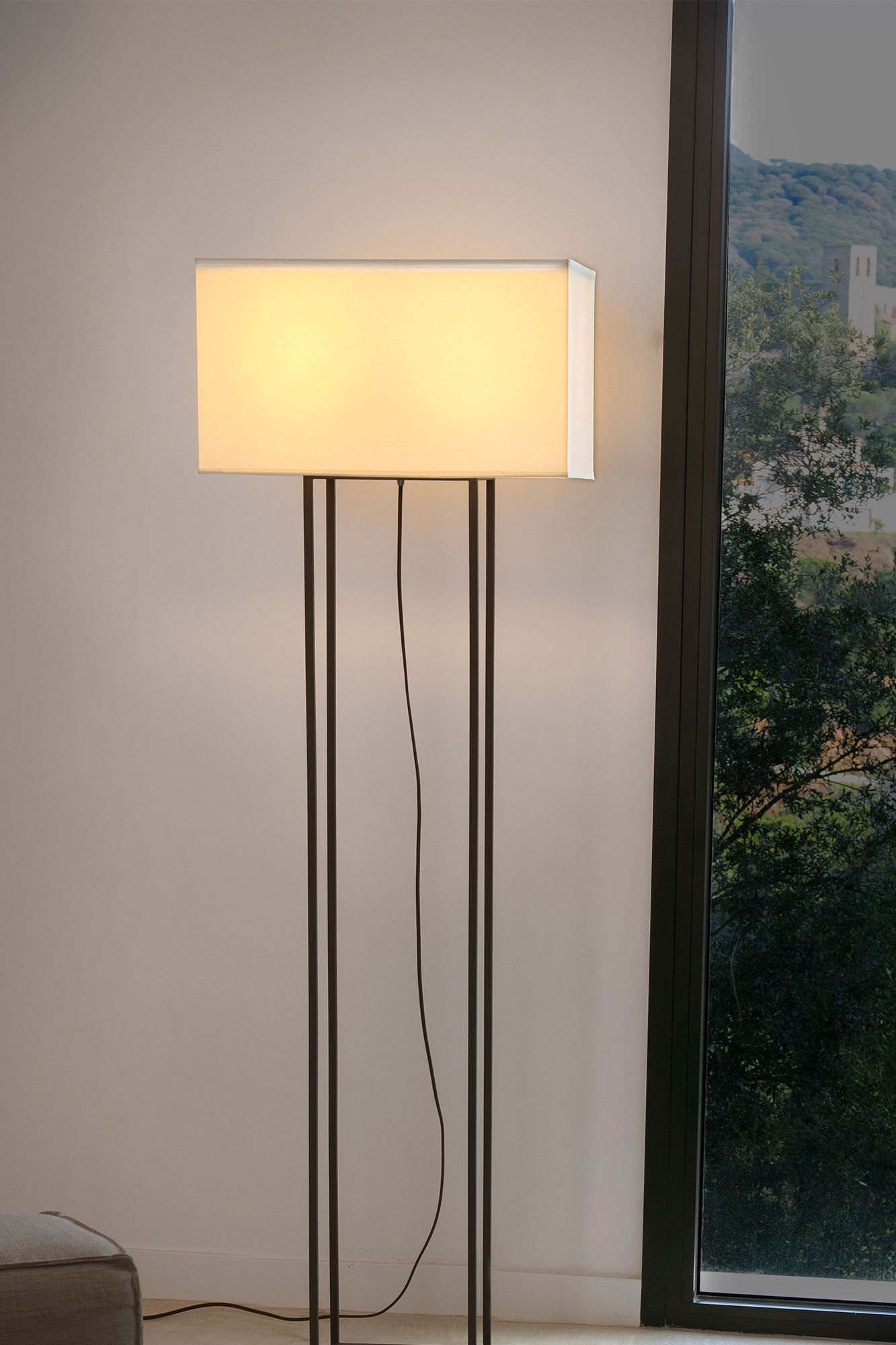 Una lampada da terra rettangolare con paralume bianco e struttura nera, vicino a una finestra.