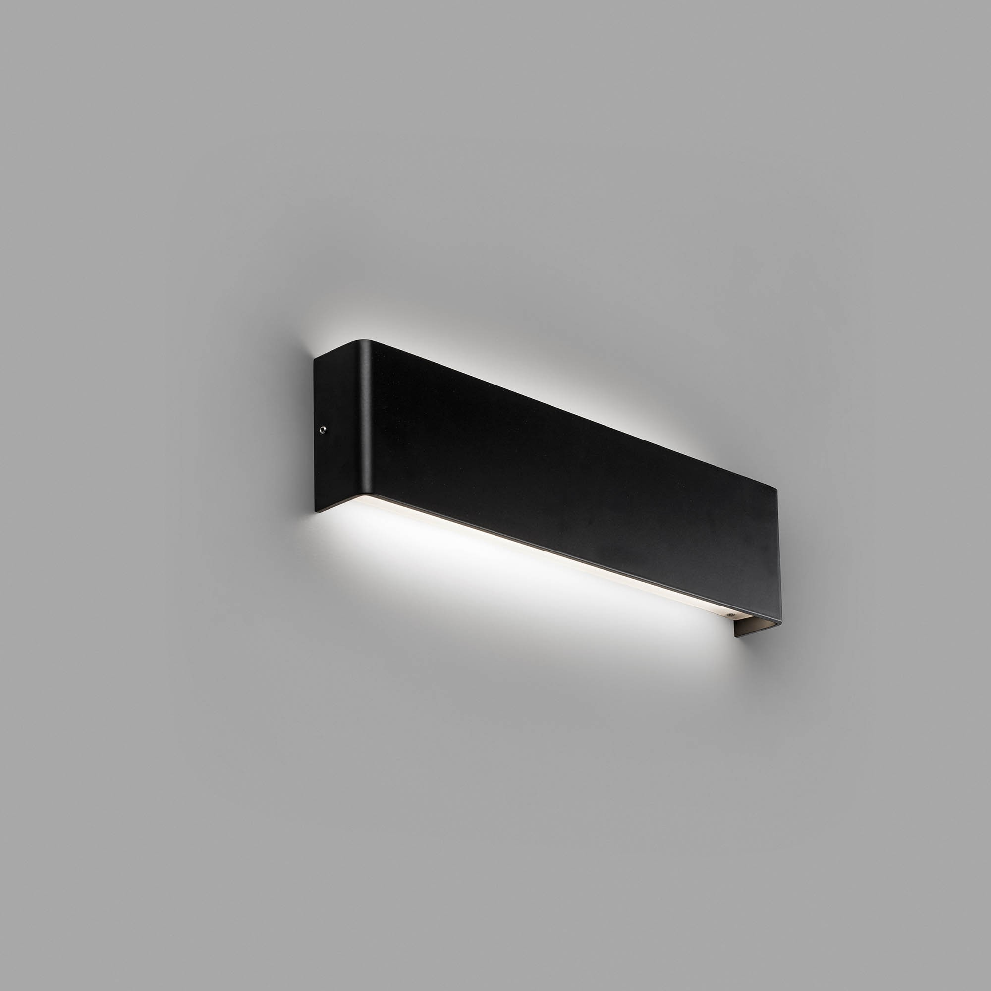 Una lampada da parete rettangolare nera che emette luce bianca. La lampada è montata su un muro grigio.