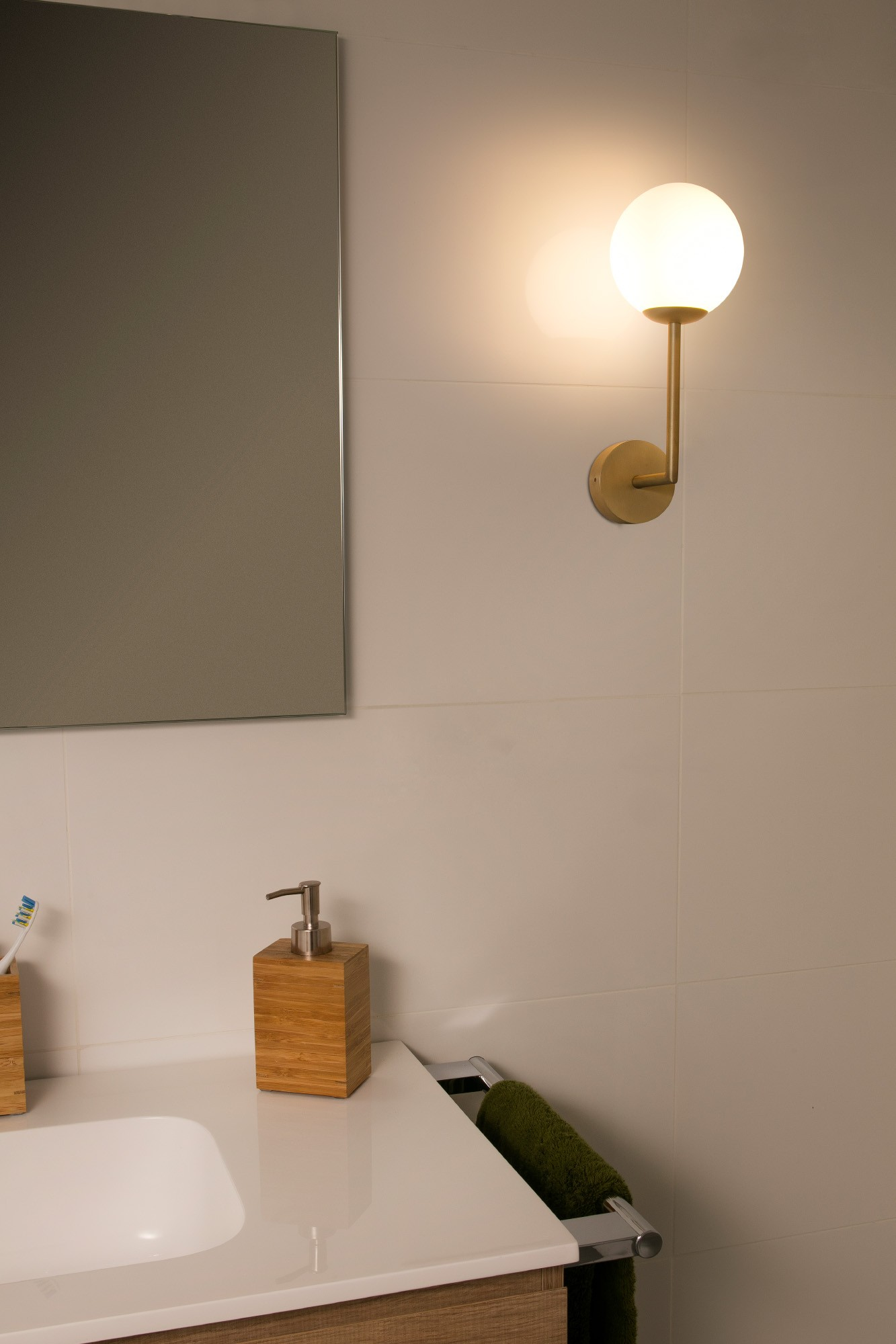 Una scena del bagno con un'applique, uno specchio e un dispenser di sapone. Il muro è bianco.