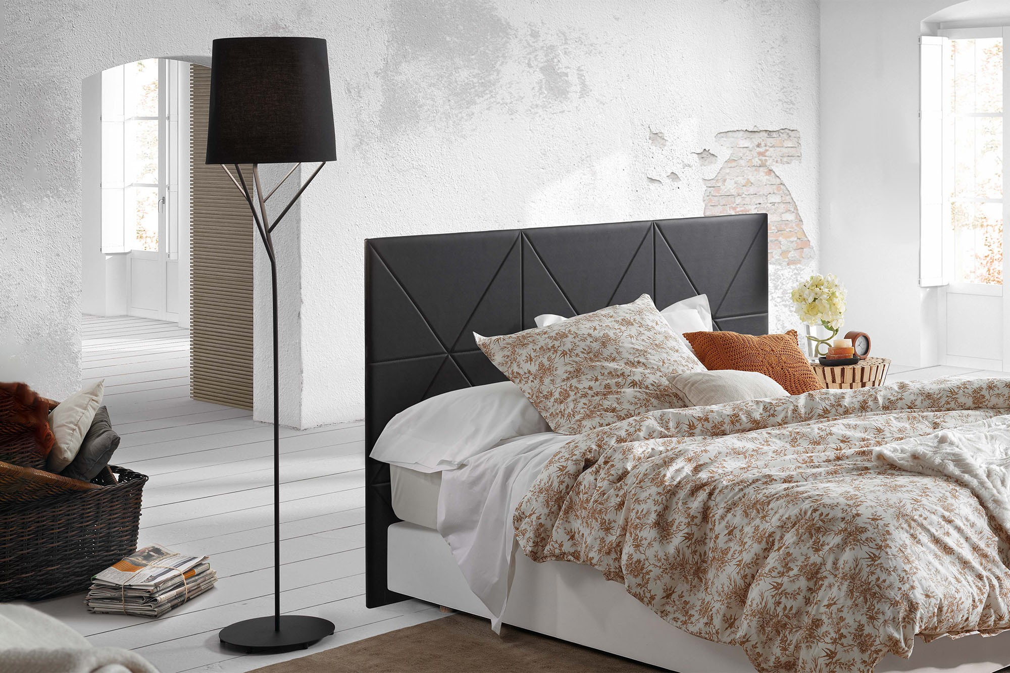 Una camera da letto con un letto, una lampada da terra e un piumino a fantasia floreale. Il muro è bianco, con texture.