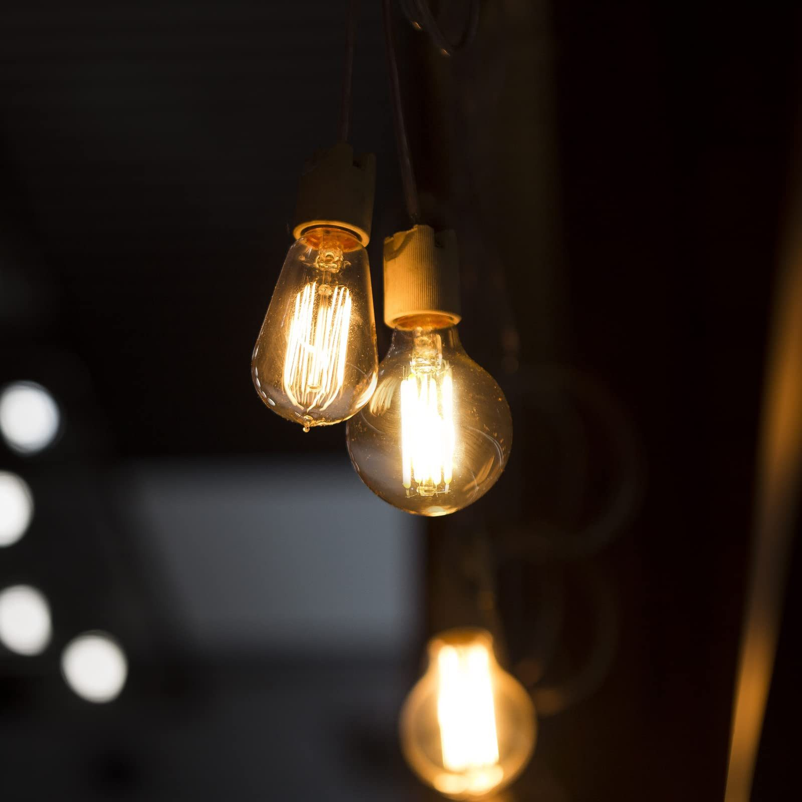 Trzy świecące żarówki zwisające z sufitu. Ciemne tło.