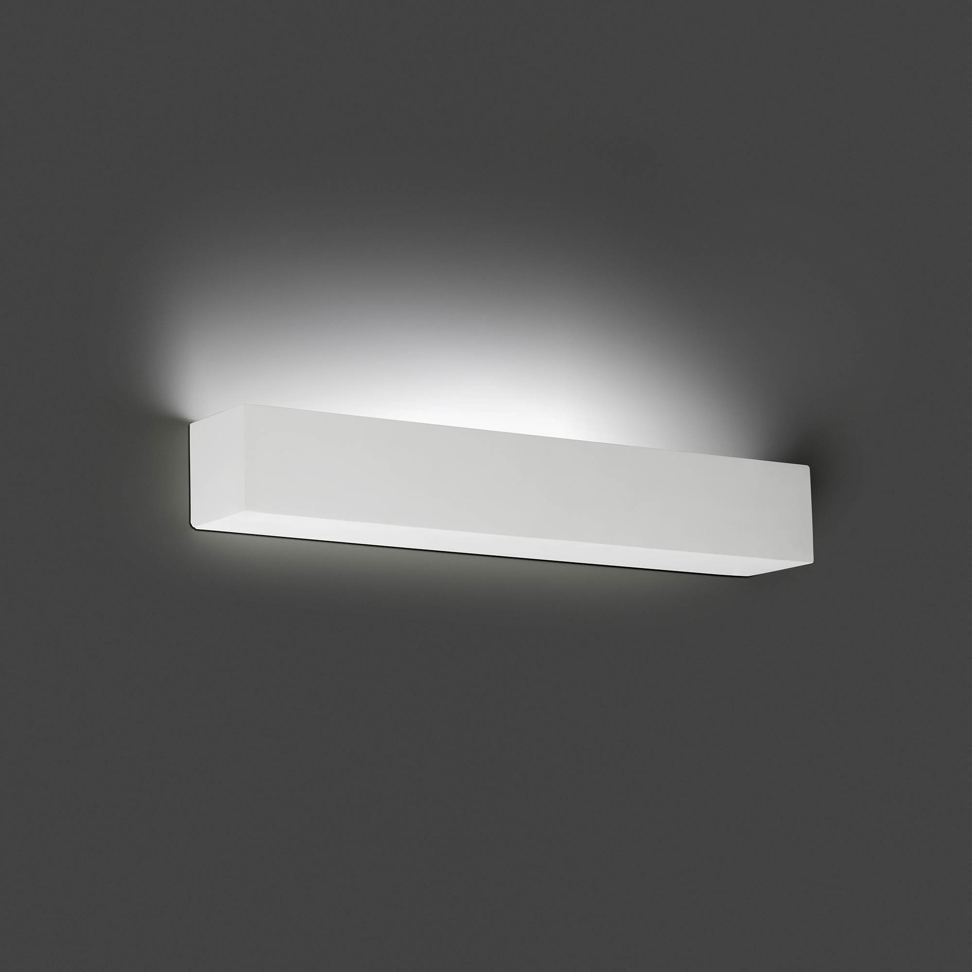 Apparecchio rettangolare bianco su parete grigia, che emette luce intensa.