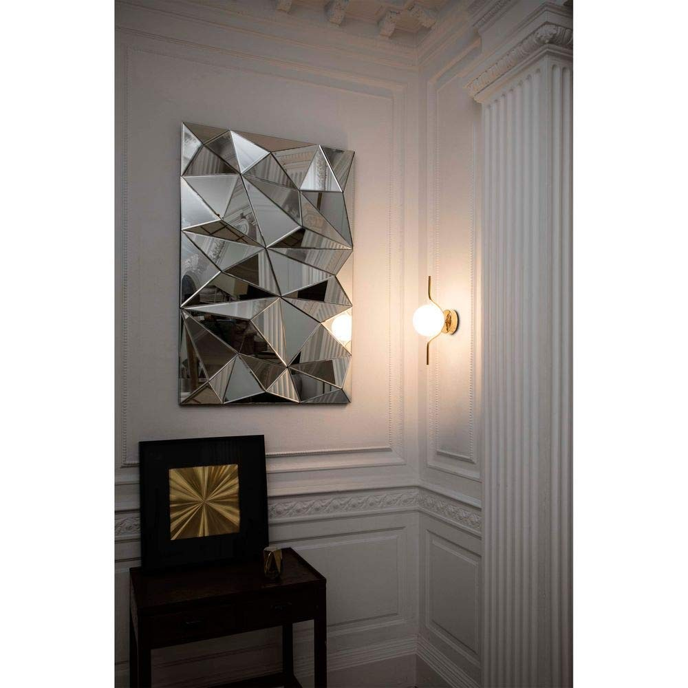 Specchio geometrico su una parete con un tavolino e una lampada da parete. La stanza è decorata con modanature.