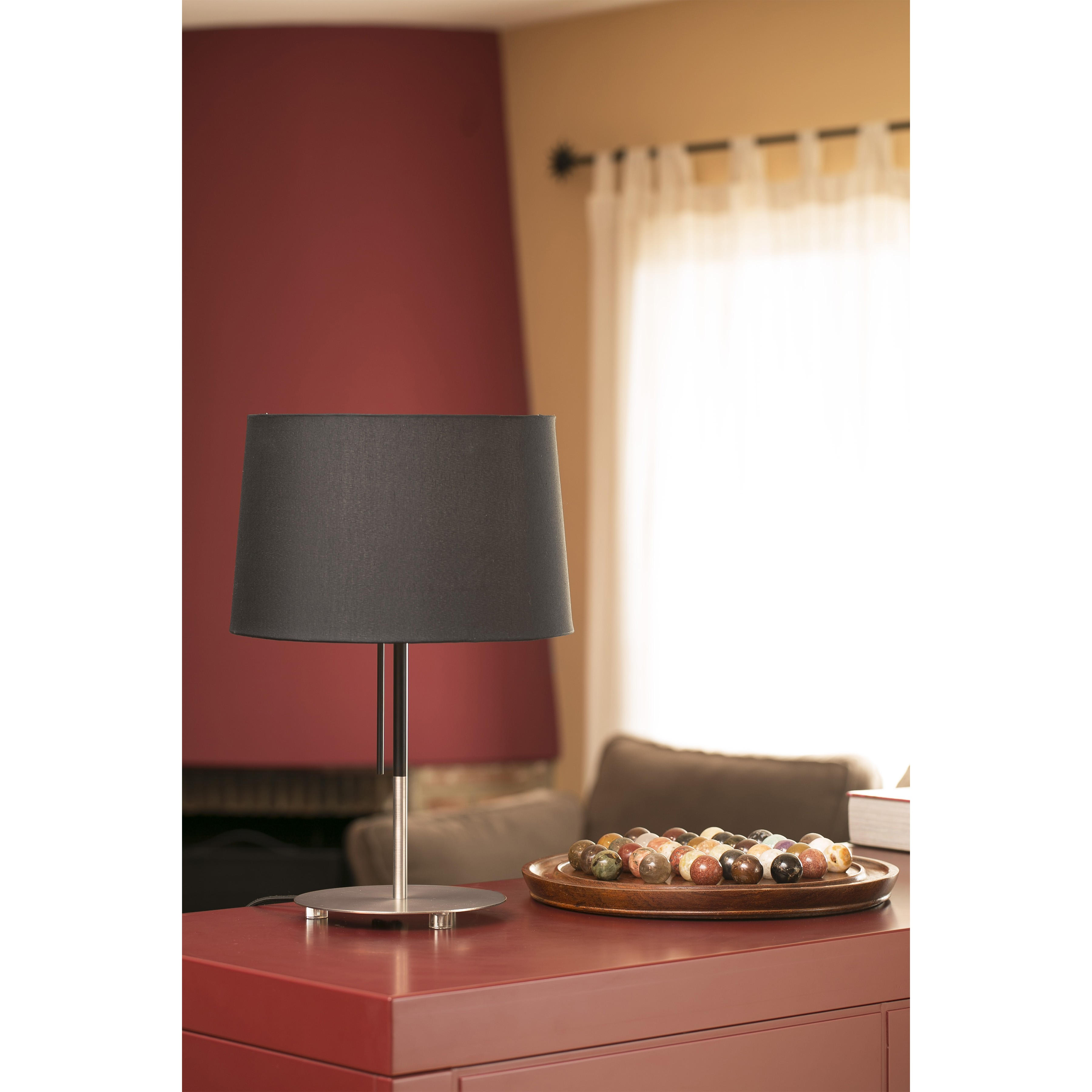 Lampada da tavolo con paralume nero e base argentata. Su un mobile rosso. Vassoio di legno con cibo.