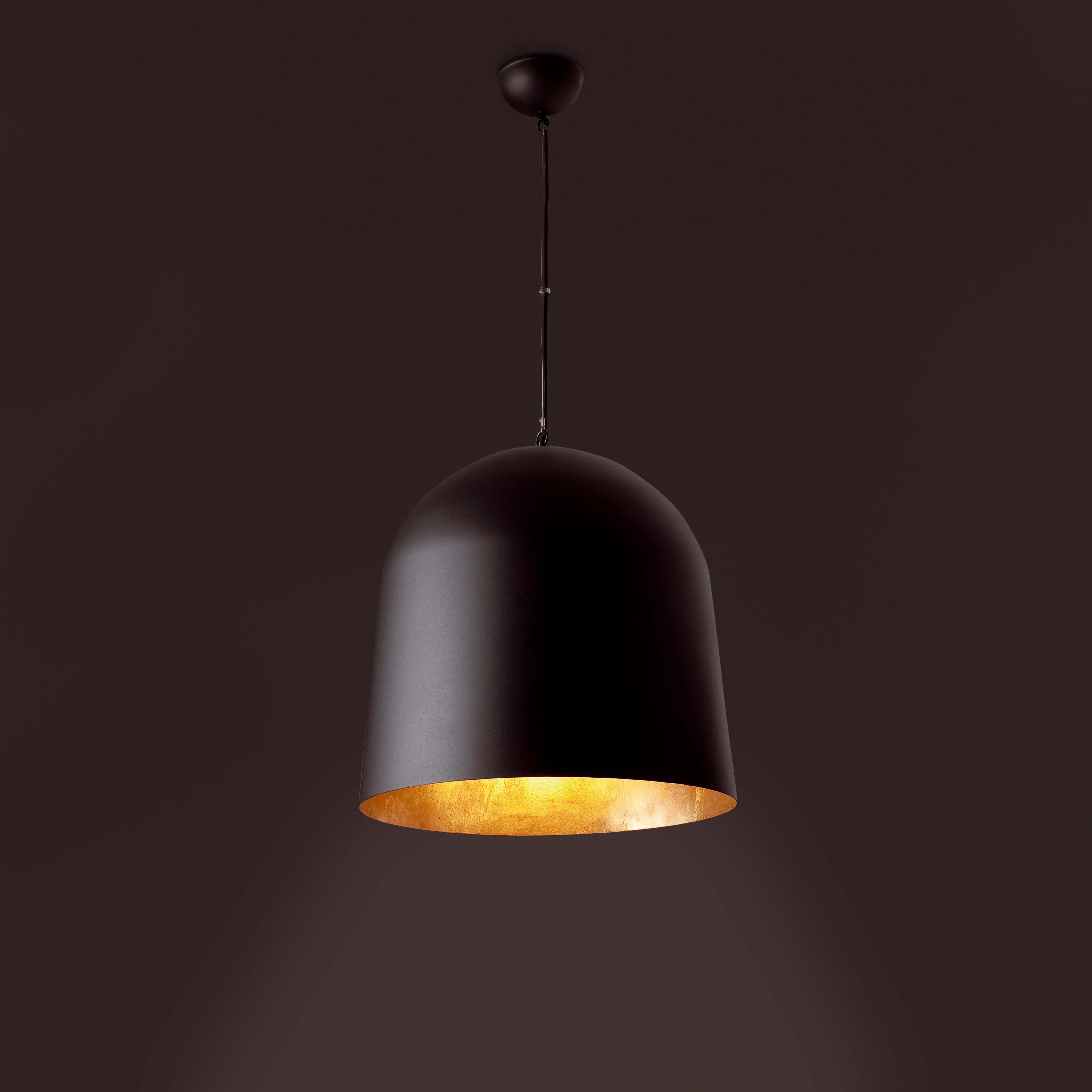 Una lampada a sospensione nera con interno dorato, sospesa su uno sfondo marrone scuro.